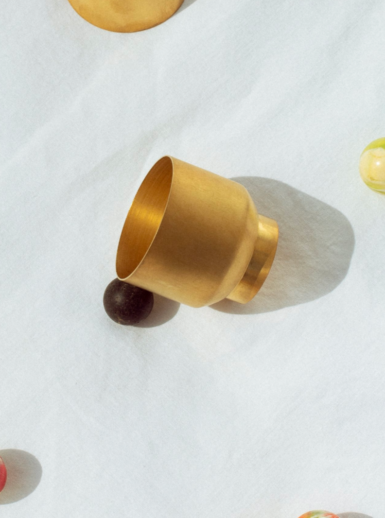 The LAVA CUP by Natalia Criado sits elegantly on a white fabric backdrop, encircled by vibrant marbles. Sunlight gently casts a soft shadow, creating a warm, serene composition with contemporary flair.