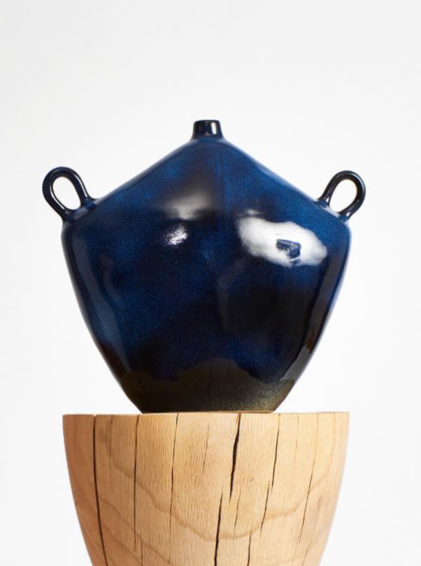 A Maria Vessel in Midnight Blue from Project 213A, with a textured shiny glaze and two handles, balanced on a wooden cylindrical base, set against a white background.