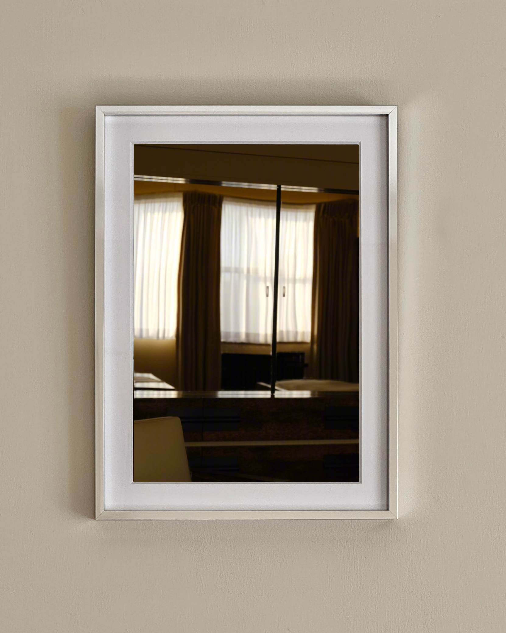 Grace Rose Watts’ Villa Cavrois; Master Bedroom - Print Photography captures a framed mirror reflecting a window with sheer curtains and brown drapes on a beige wall, softly illuminated in this limited edition artwork.