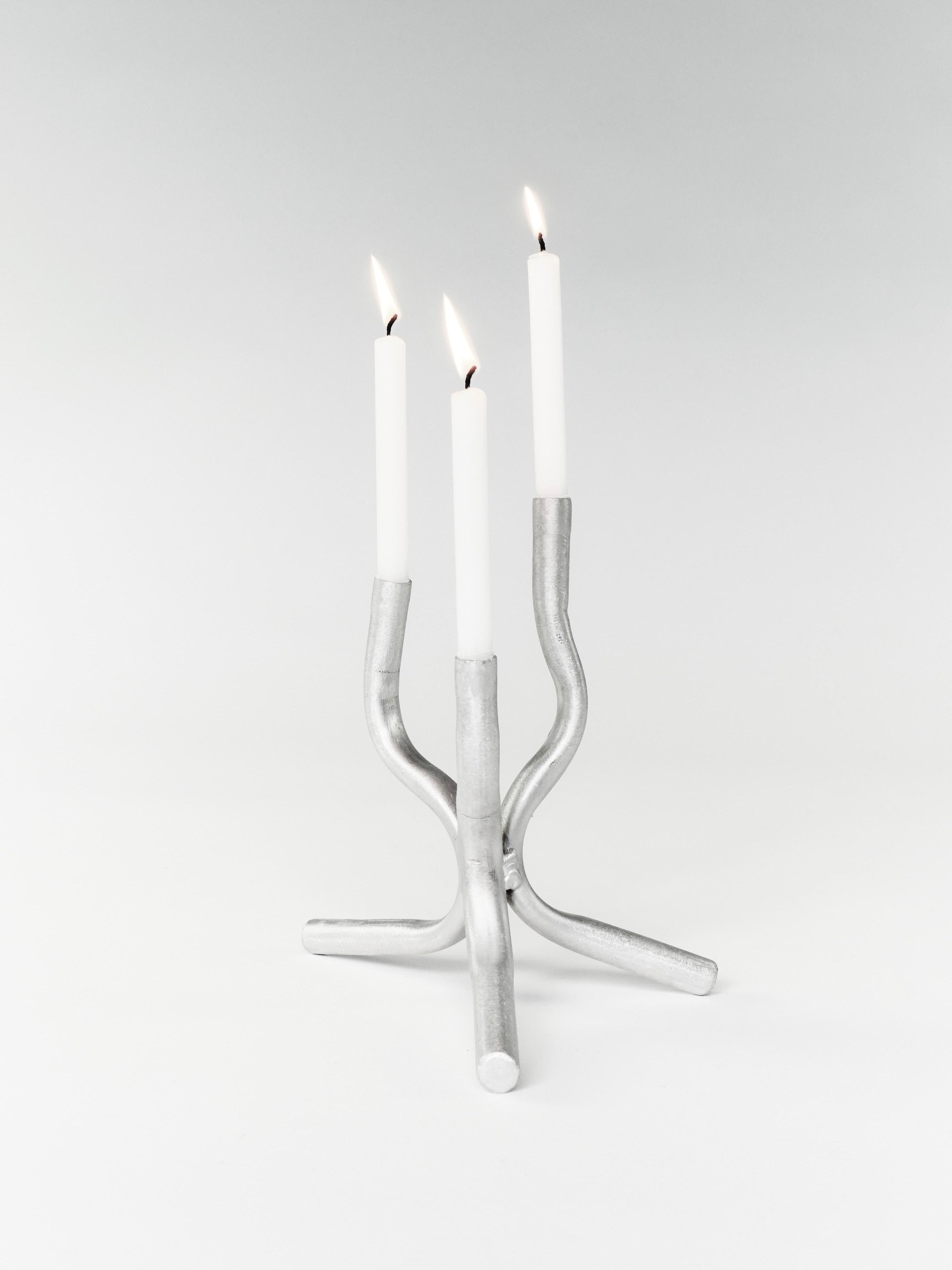 The Six Dots Design Mini Candelabra, handcrafted in a North London workshop, showcases a modern, curved design holding three lit white candles against a plain background.