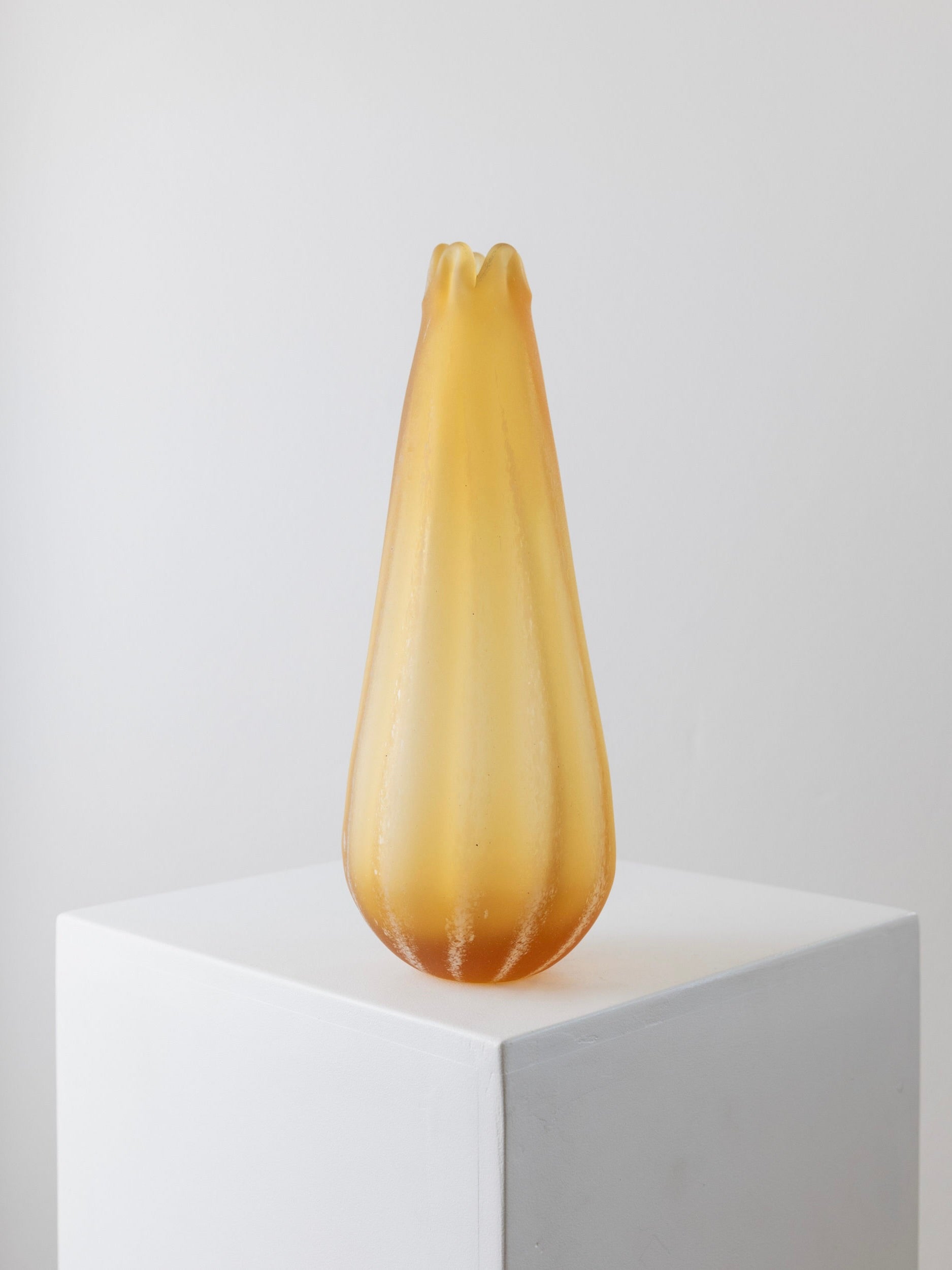 A pear-shaped, translucent, amber-colored glass vase from the 1960s Murano collection by Bottega Jacobs is displayed on a white pedestal against a plain background. The Large Murano Glass Vase - Italy 1960s boasts a smooth, glossy surface with subtle contour lines, making it a striking decorative highlight.