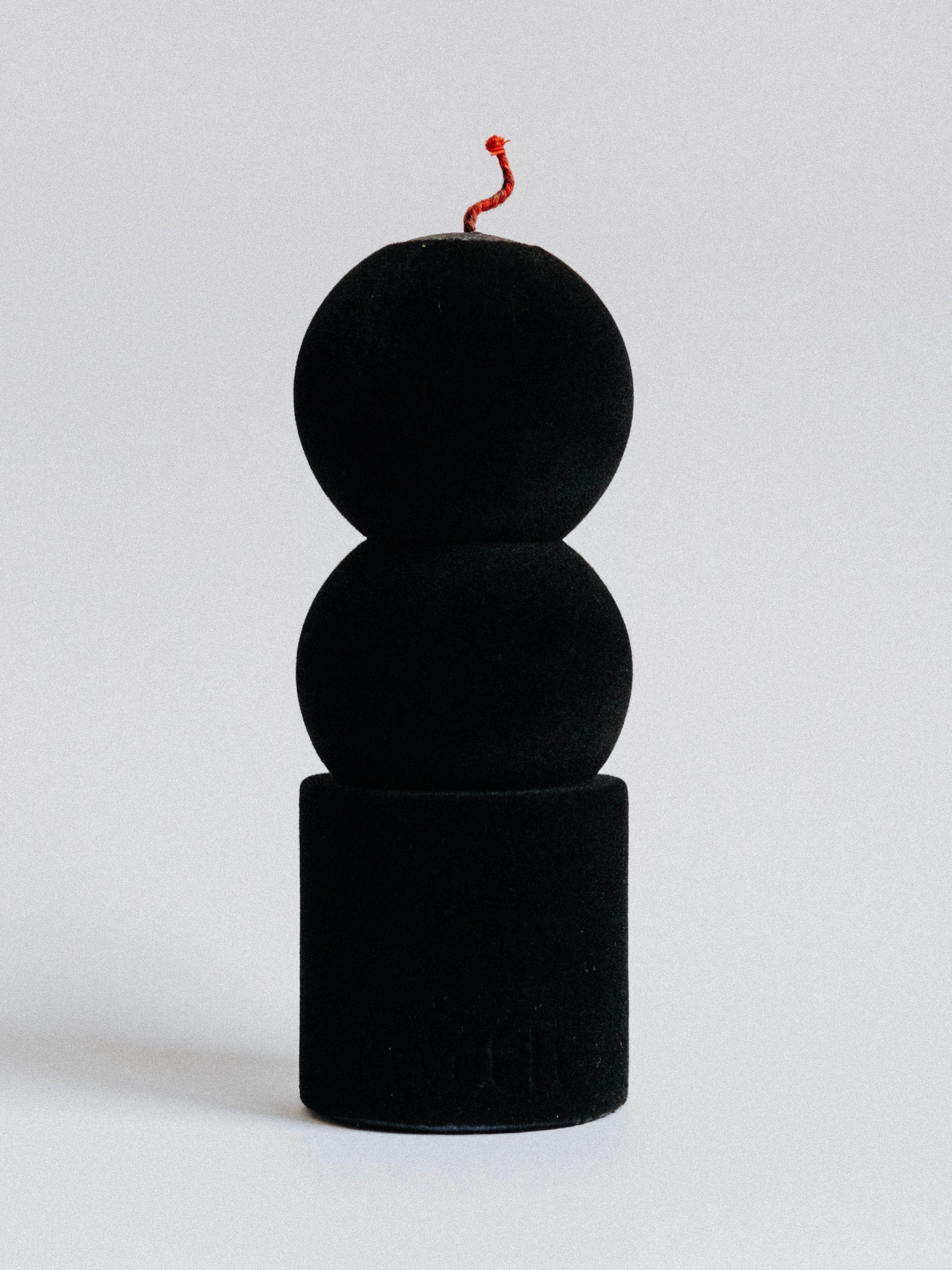 The Lilu Candle Black Velvet Edition by Taith features three stacked black spheres with a red wick on top, resembling a minimalist bomb sculpture. Made from natural soy wax, it adds an eco-conscious touch against the plain white background.