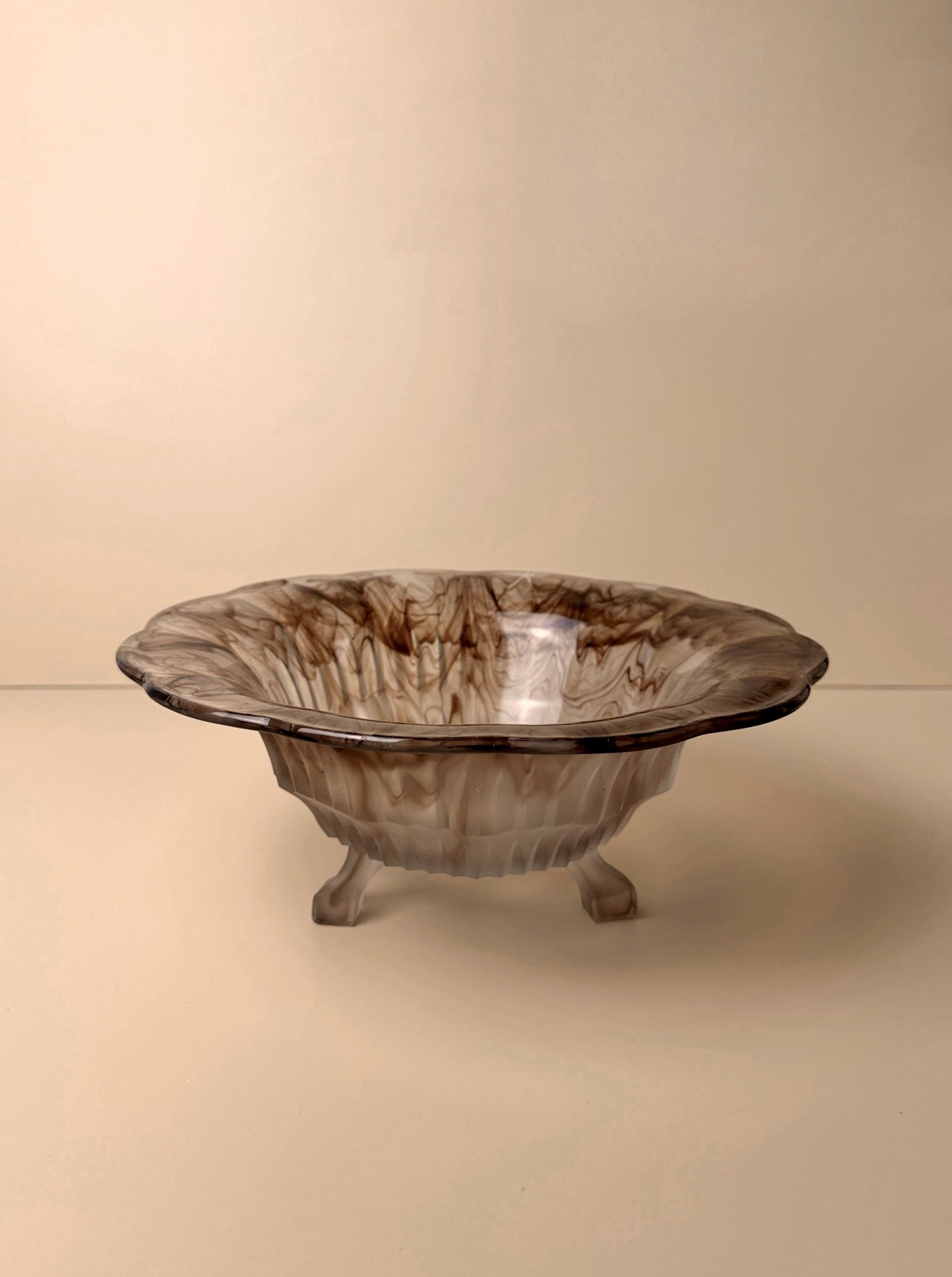 The Dodo Vintage German Art Deco Cloud Glass Foot Bowl, a round, shallow ceramic piece with three small legs, is displayed against a beige background. Reminiscent of 1930s German Art Deco Cloud Glass, it boasts a marbled brown and beige pattern that gives it a textured, artistic appearance.