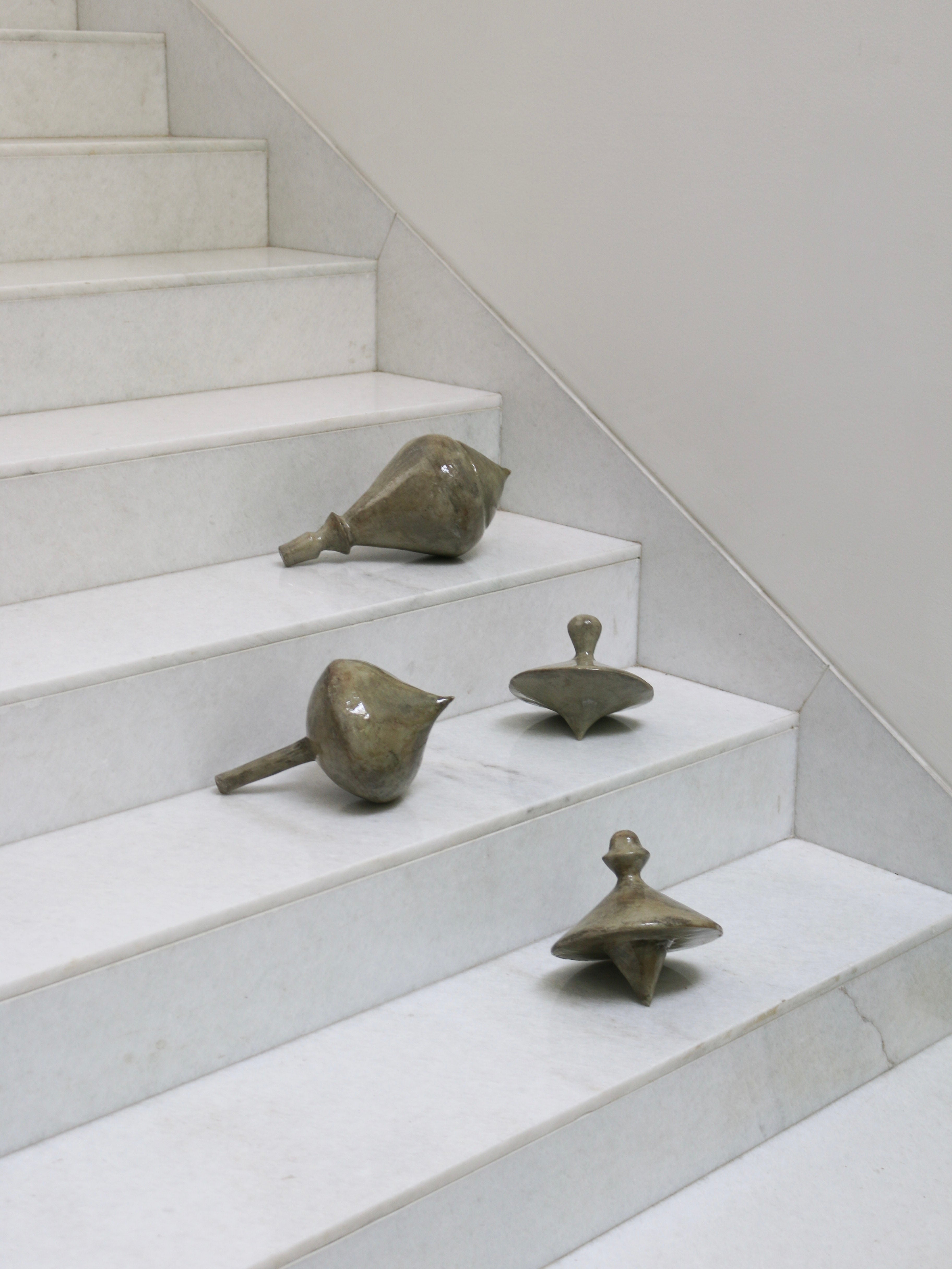 Set of four olive green ceramic spinning top sculptures on marble stairs