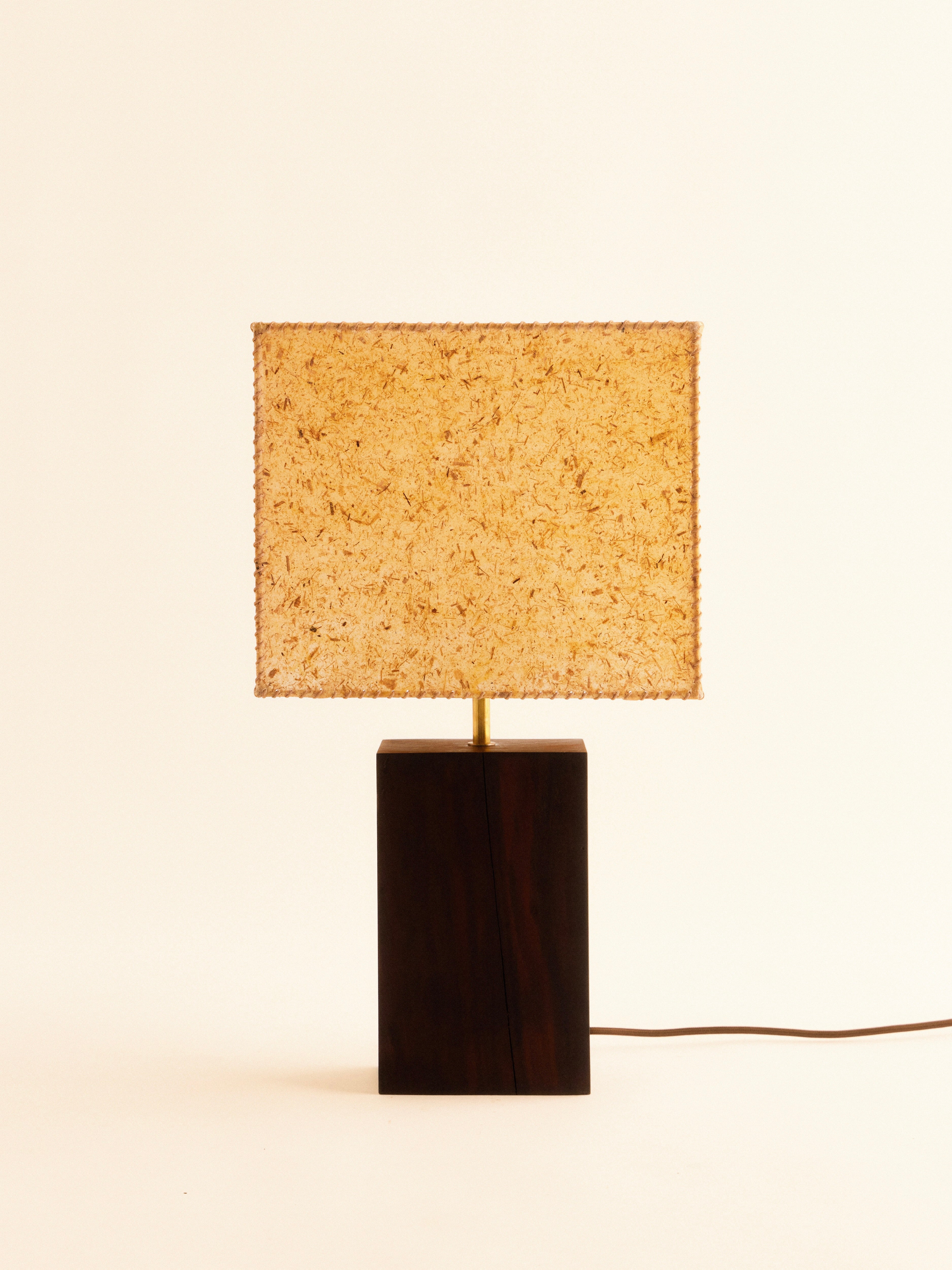 The 1948 Table Lamp by Lana Launay, handcrafted in Sydney, features a dark wooden rectangular base and is topped with a textured banana fibre square shade. Set against a plain light background, its design includes a visible power cord extending from the base.