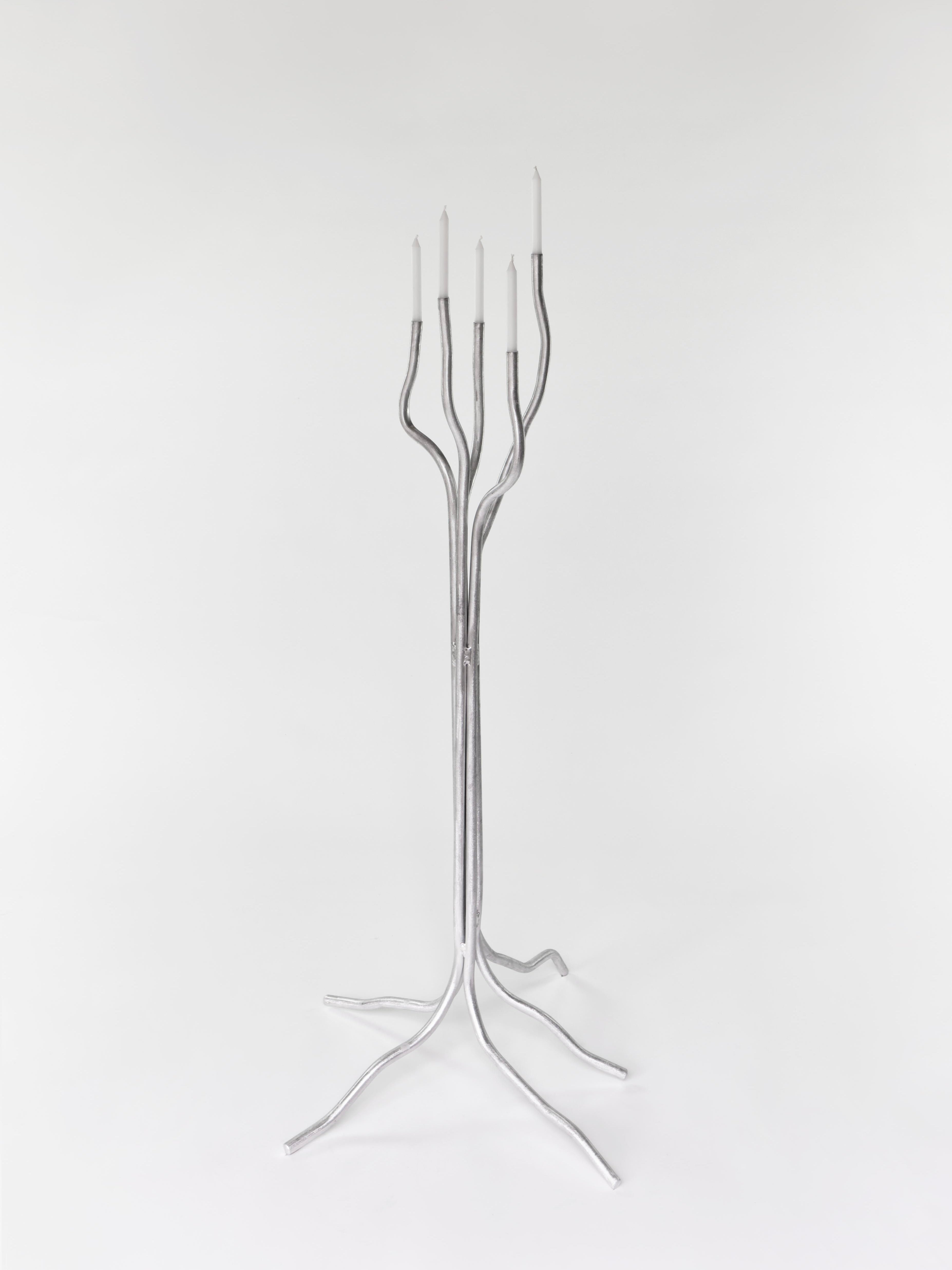 The Tall Aluminum Candelabra by Six Dots Design is a modern, artistic piece with multiple branches. This handcrafted item from a North London workshop features sleek curved arms holding lit candles, standing elegantly against a white background.