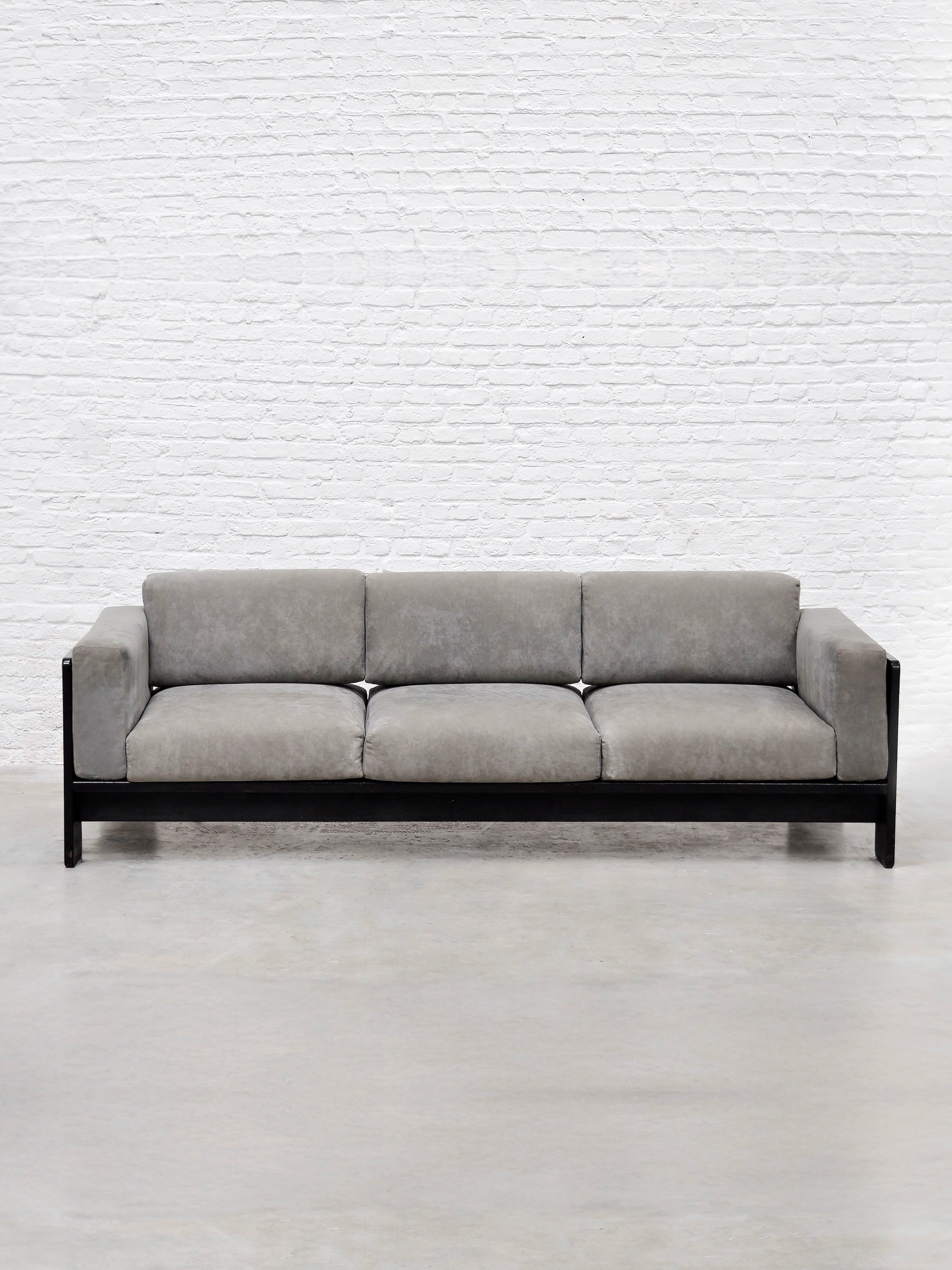 A modernist setting showcases the Bastiano Sofa by Tobia Scarpa for Gavina, 1960s, from Introverso. It features sleek gray suede cushions against a white brick wall with a smooth, light gray floor for a contemporary look.