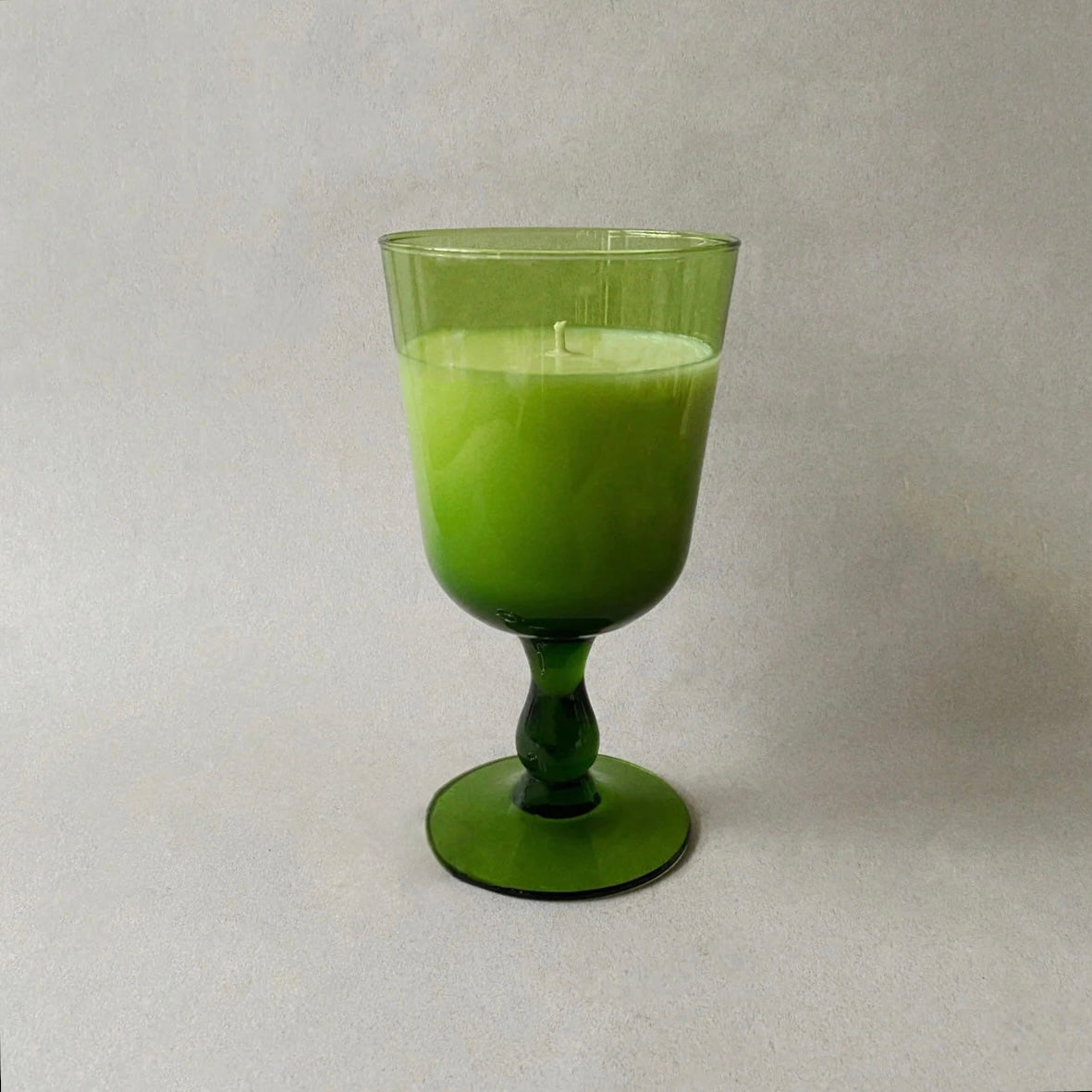 A Big Green Glass Candle soy wax candle on a gray background. The candle is partially used, with visible wax around the wick at the center.