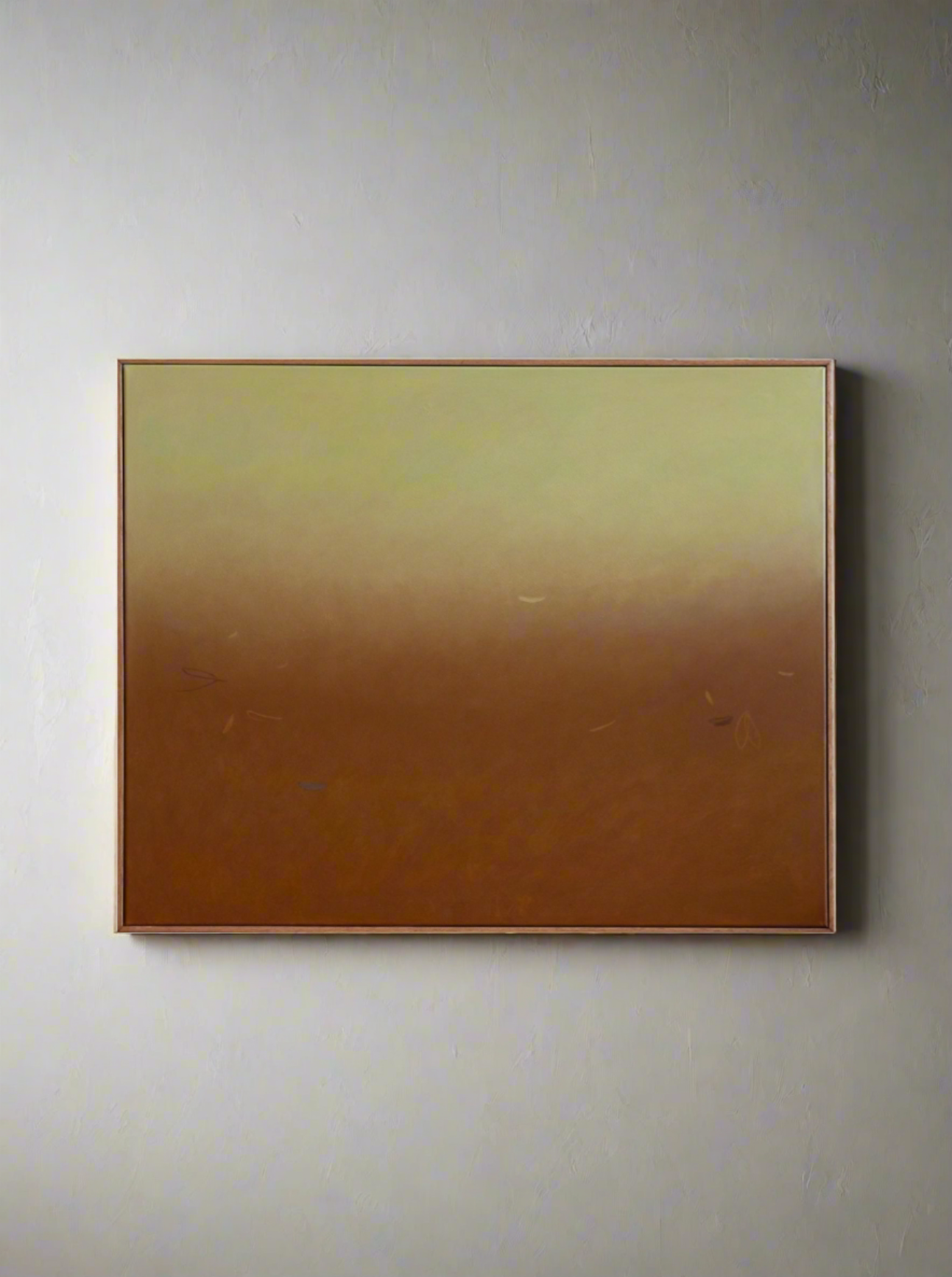A rectangular painting featuring a gradient that transitions smoothly from a soft green at the top to a deep brown at the bottom. There are faint, abstract lines and shapes in various colors scattered throughout the brown area. The acrylic on canvas artwork, titled "Something(s) in the air, 2024" by Rebecca von Matérn, is elegantly framed with an oak frame.