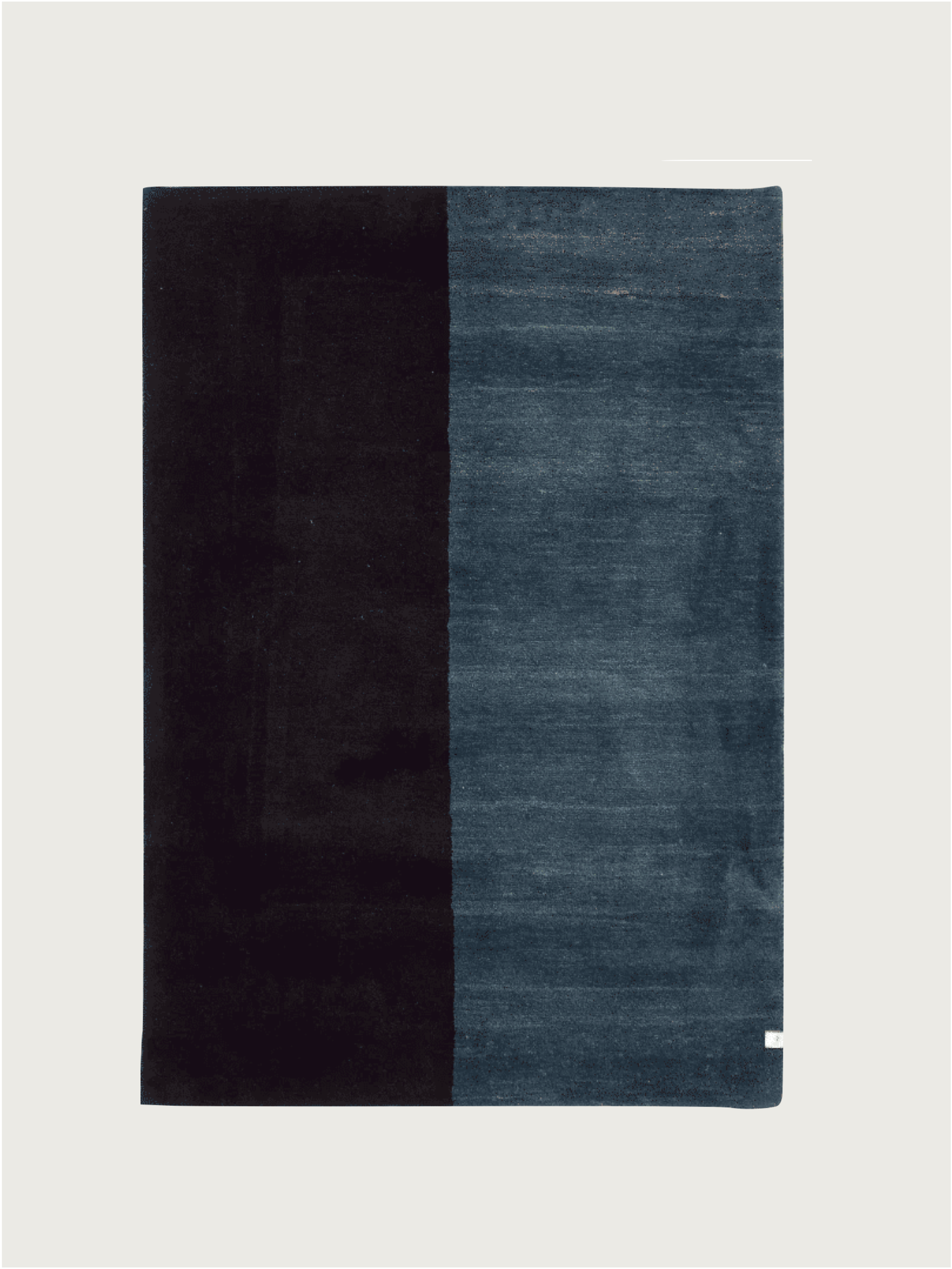 The Gabbeh Rug in Cobalt by catalog:three is a rectangular, hand-knotted piece with a modern, minimalistic design. It showcases two vertical halves: solid black and muted dark blue, featuring a subtle texture and a small white tag in one corner. Size is 94 x 177 cm.