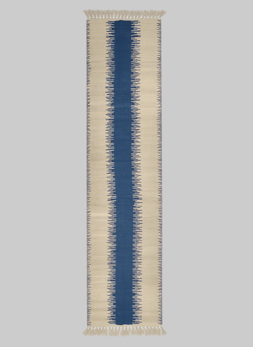 A long, rectangular Navy Anar Kilim Runner - Handwoven Rug by ISHKAR with a jagged, symmetrical pattern runs vertically down the center. This handwoven wool rug features a wide central blue stripe flanked by narrower cream-colored stripes with irregular, serrated edges, all created using natural dyes that blend into the background.