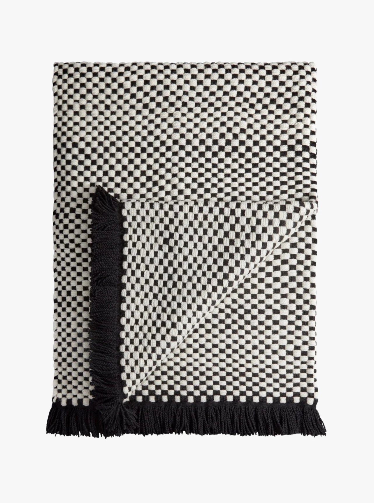 The Damier Throw - Black by LOBJET, featuring a black and white checkered design with fringed edges, artistically folded to showcase both sides, adds a sculptural touch to any luxury interior.