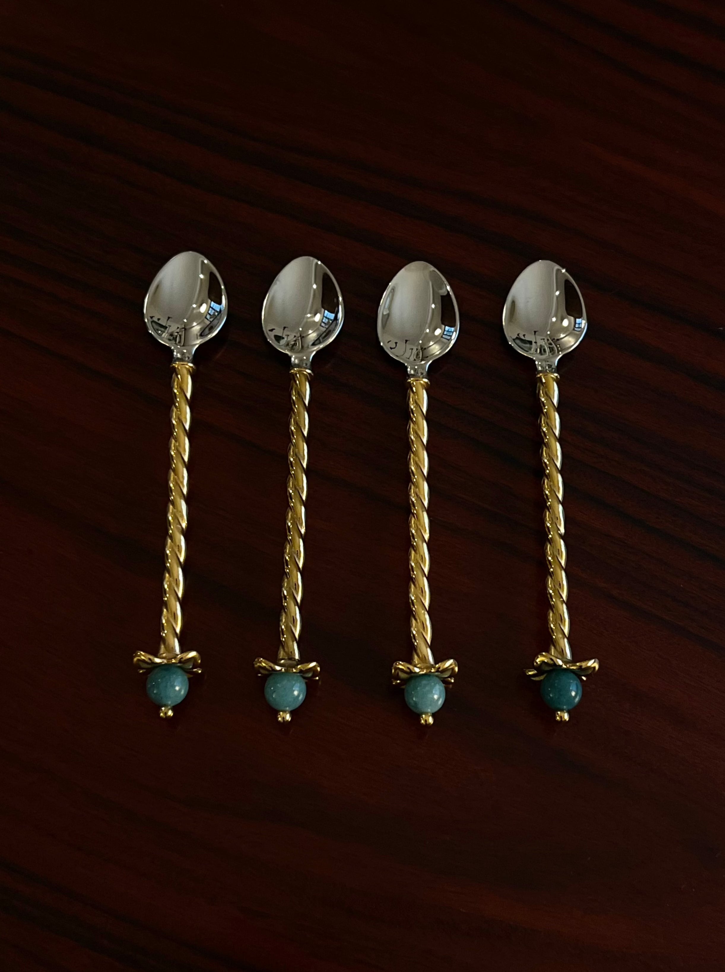 Four LOBJET Venise Dessert Spoons, featuring twisted gold handles and teal stone accents, are artfully arranged parallel on a dark wooden surface, showcasing a contemporary design that enhances any dining experience.
