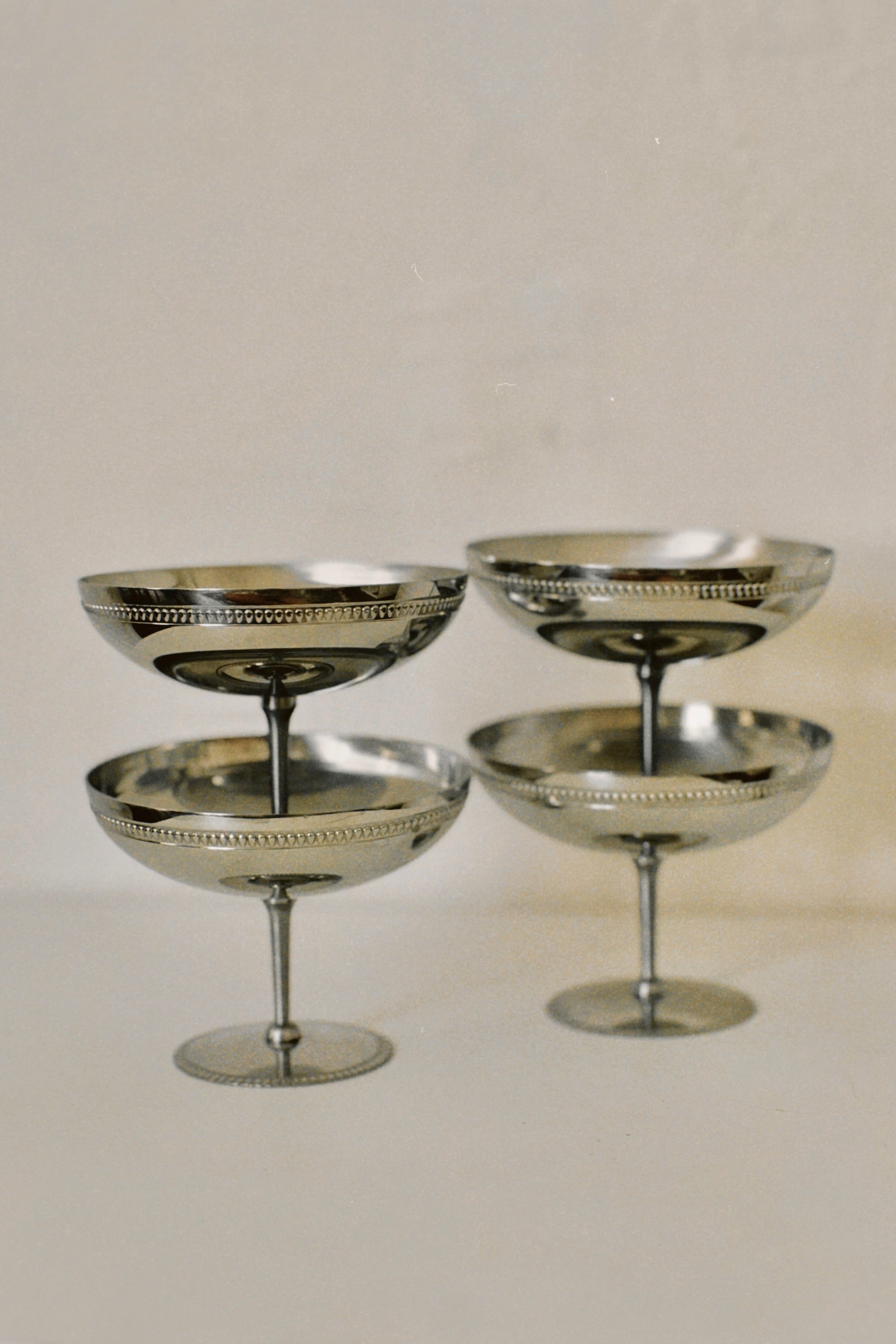 Four Set of 4 Silver Ice Cream Coupes with intricate stem designs arranged in a staggered formation on a light background, perfect for a luxurious dining experience by Manushi.