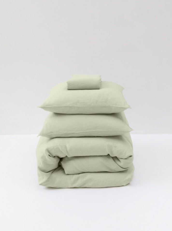 A stack of neatly folded MOST Washed Linen Bed Set in Sage, including sheets and pillowcases, set against a plain white background.