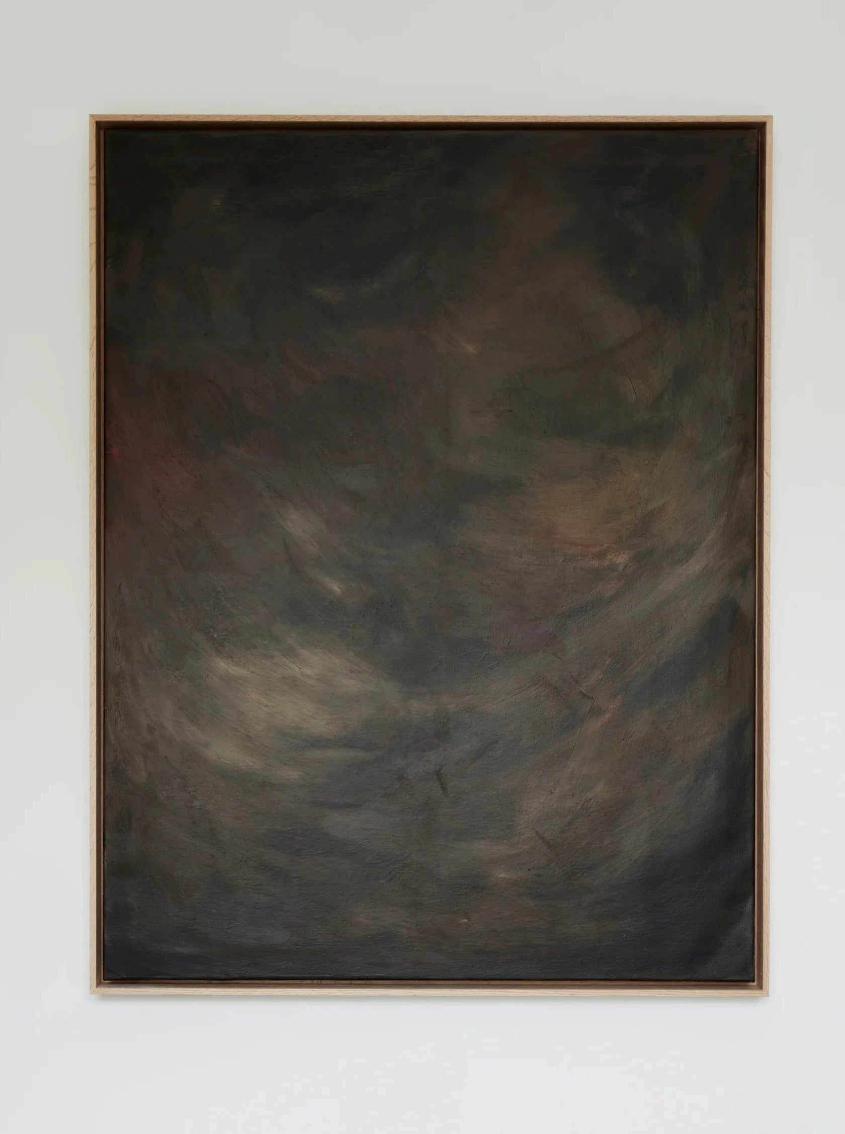 A framed abstract painting hangs on a white wall. The mixed media artwork features a dark, swirling mix of earthy colors, including shades of black, brown, and hints of green, with indistinct shapes and textures creating a mysterious, moody atmosphere. Shadowed Abyss - Mixed media on canvas by Mattias Storm is encased in an elegant oak frame.