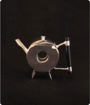 Vintage silver teapot with a circular body and black handle, set against a dark background.