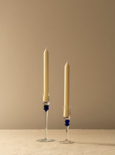 Two tall, beige candles in the Les Objets Amsterdam Memphis liquor glasses set of 5 with blue accents, standing against a soft beige background.