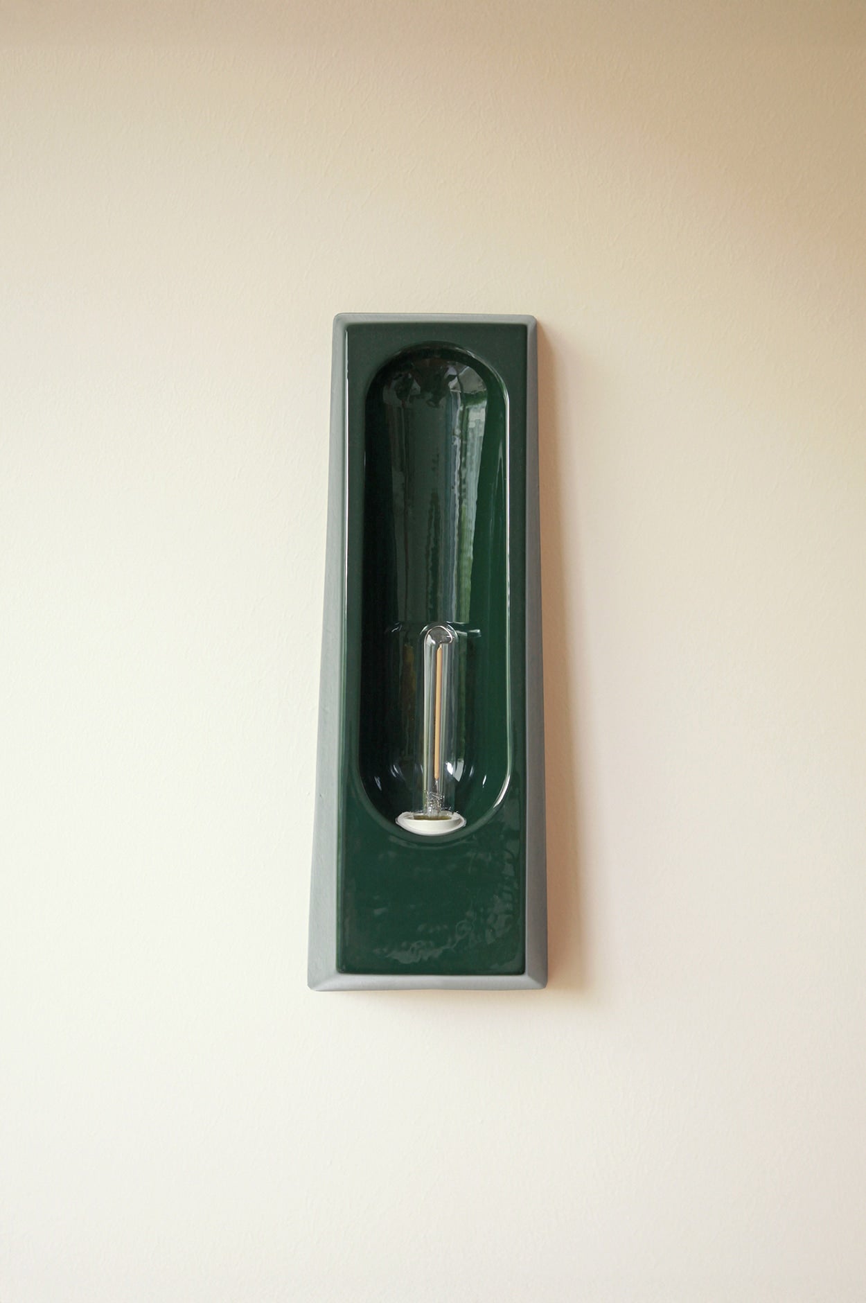 Green ceramic wall lamp with elongated Edison bulb in recessed alcove design