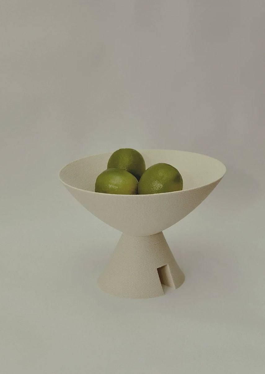 A textured white Argot Studio Budō Bowl containing four green limes on a pale background.