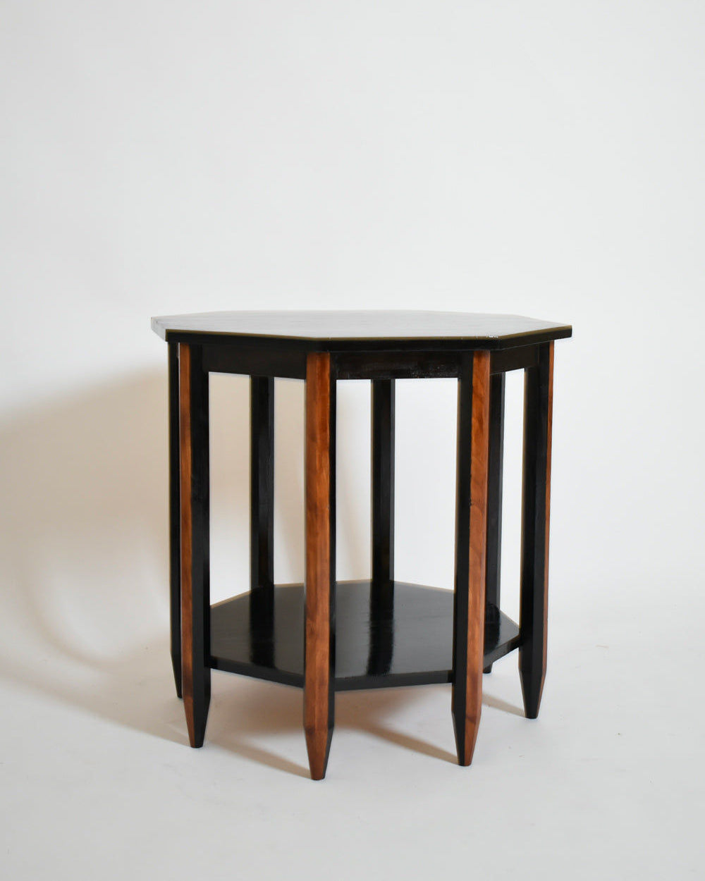The Octogonal Modernist Side Table by Barracuda Interiors (1920s) features a black top and lower shelf, six tapered natural wood legs, and is set against a plain white background.