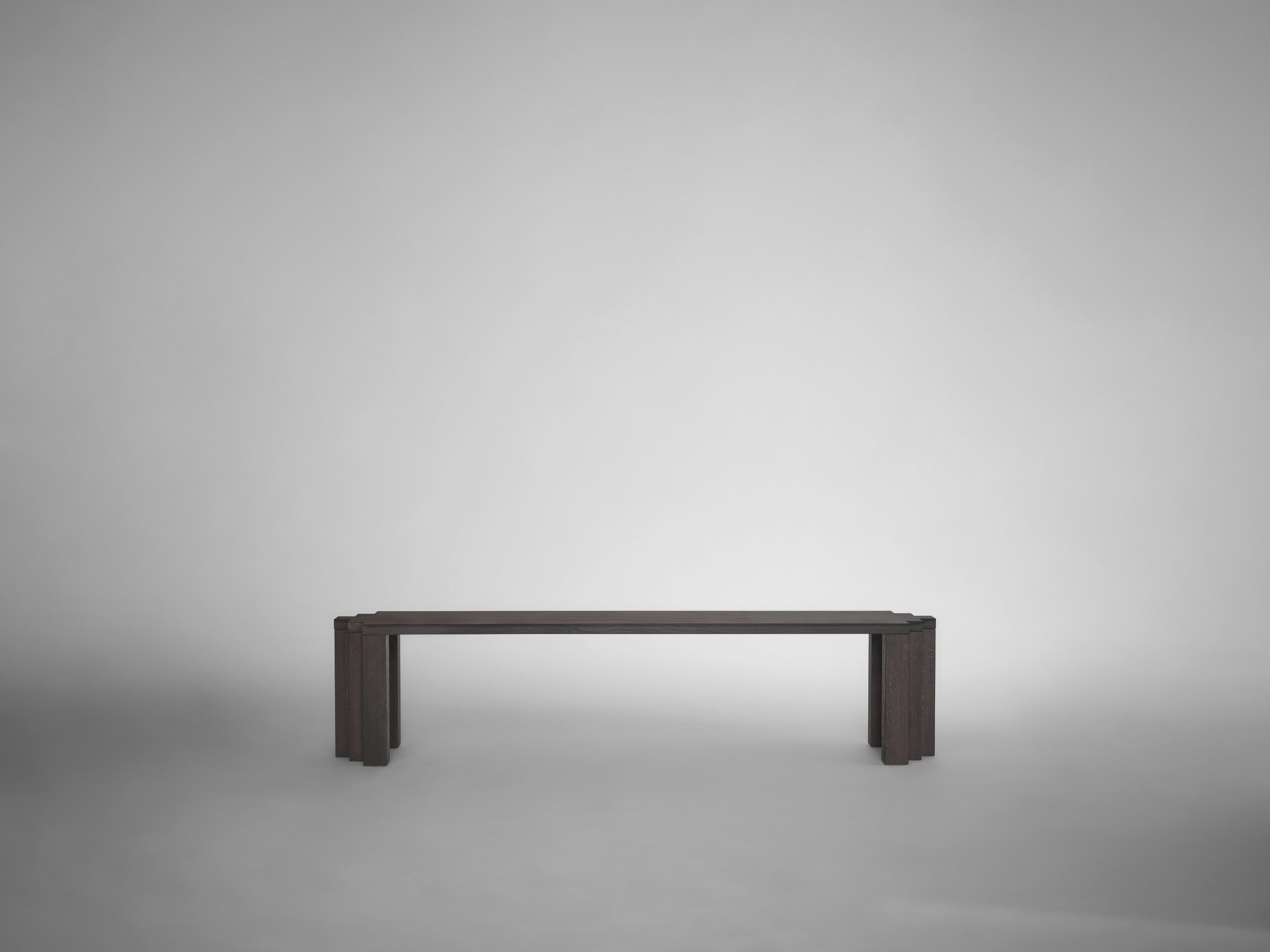 The Cadence Bench by Mokko, crafted from solid European oak, stands centered against a plain light gray background. Its minimalist, modern design features clean lines and sturdy legs, embodying the elegance of customizable furniture.