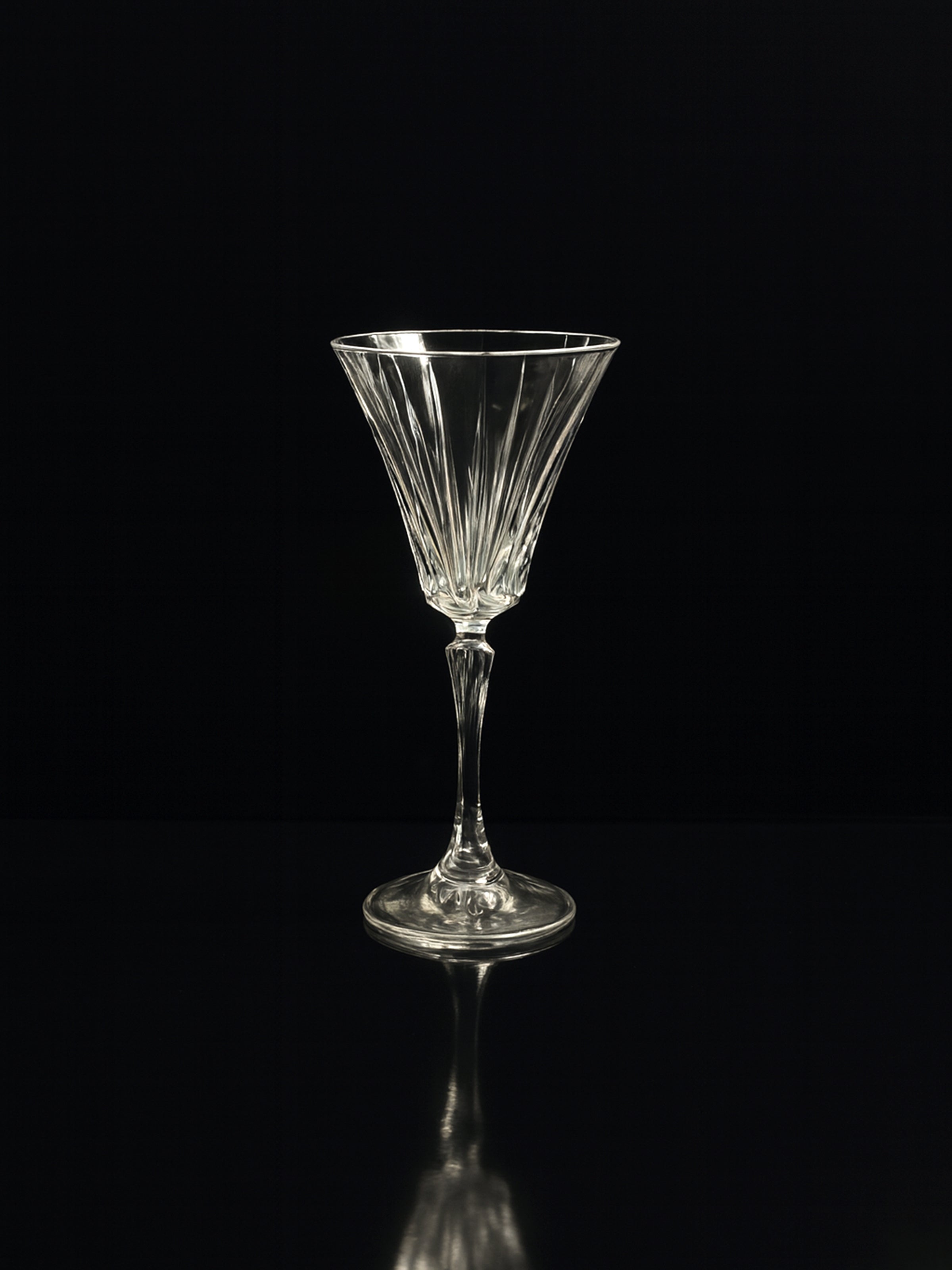 A single hand-cut Art Deco crystal glass from the Dodo Vintage Italian champagne and wine sets stands on a reflective black surface against a dark background.
