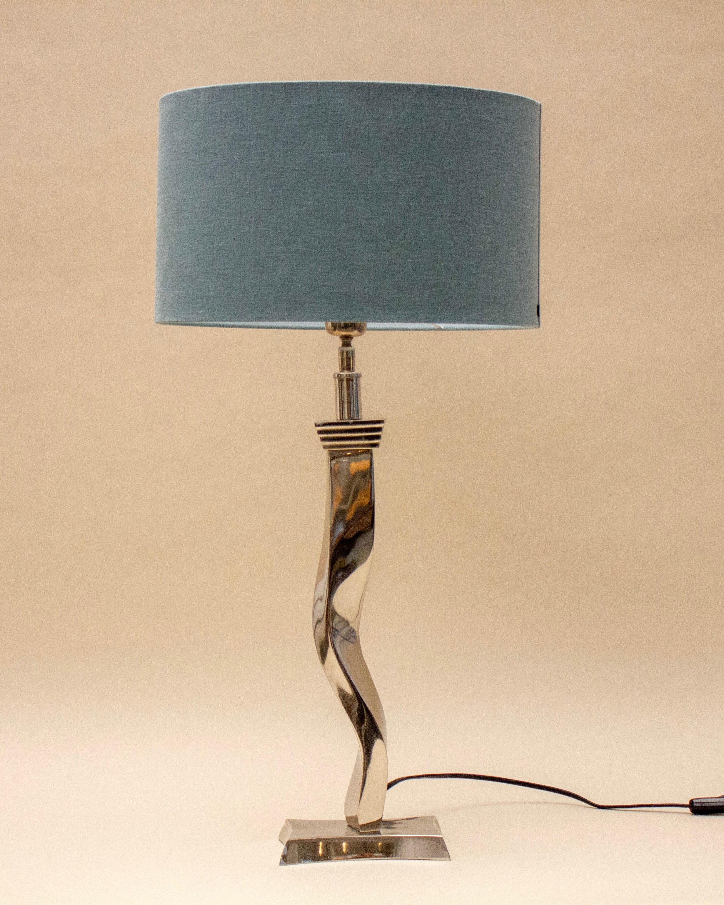 The SÒLER TAVIRA BLUE LAMP features a twisted metal base, a large sky blue lampshade, and a black power cord, perfect for adding modern style to any flat surface.
