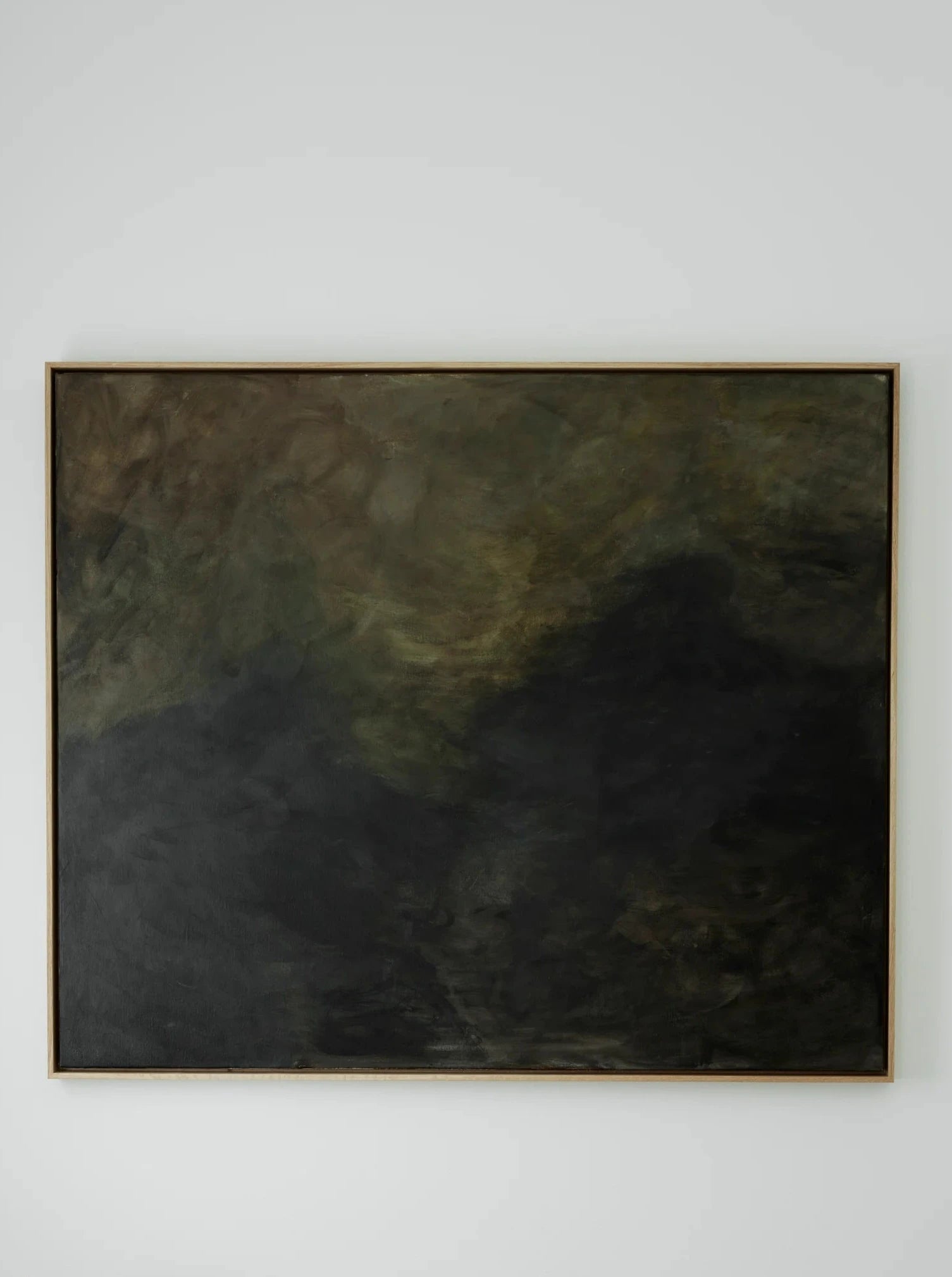 A sparse, minimalist interior features a dark, abstract painting from the Veiled Dusk - mixed media on canvas by Mattias Storm in an oak frame on a pale wall. Below the painting is a small wooden stool with a large seashell on it. On the right, a black wall-mounted candle holder with two candles and leaf details is visible.