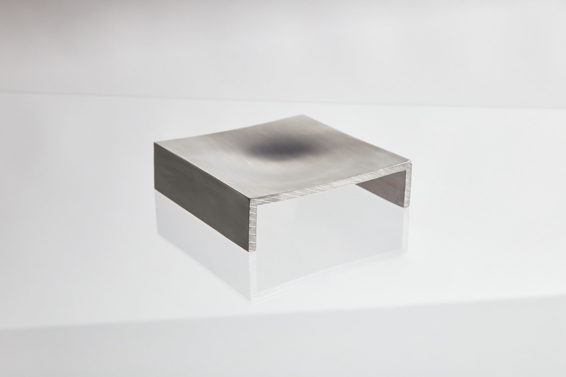 The LESORR Square Aluminum Vide-Poche, featuring a curved top and two short legs like a mini bridge, acts as a stylish small object holder on a glossy white background.