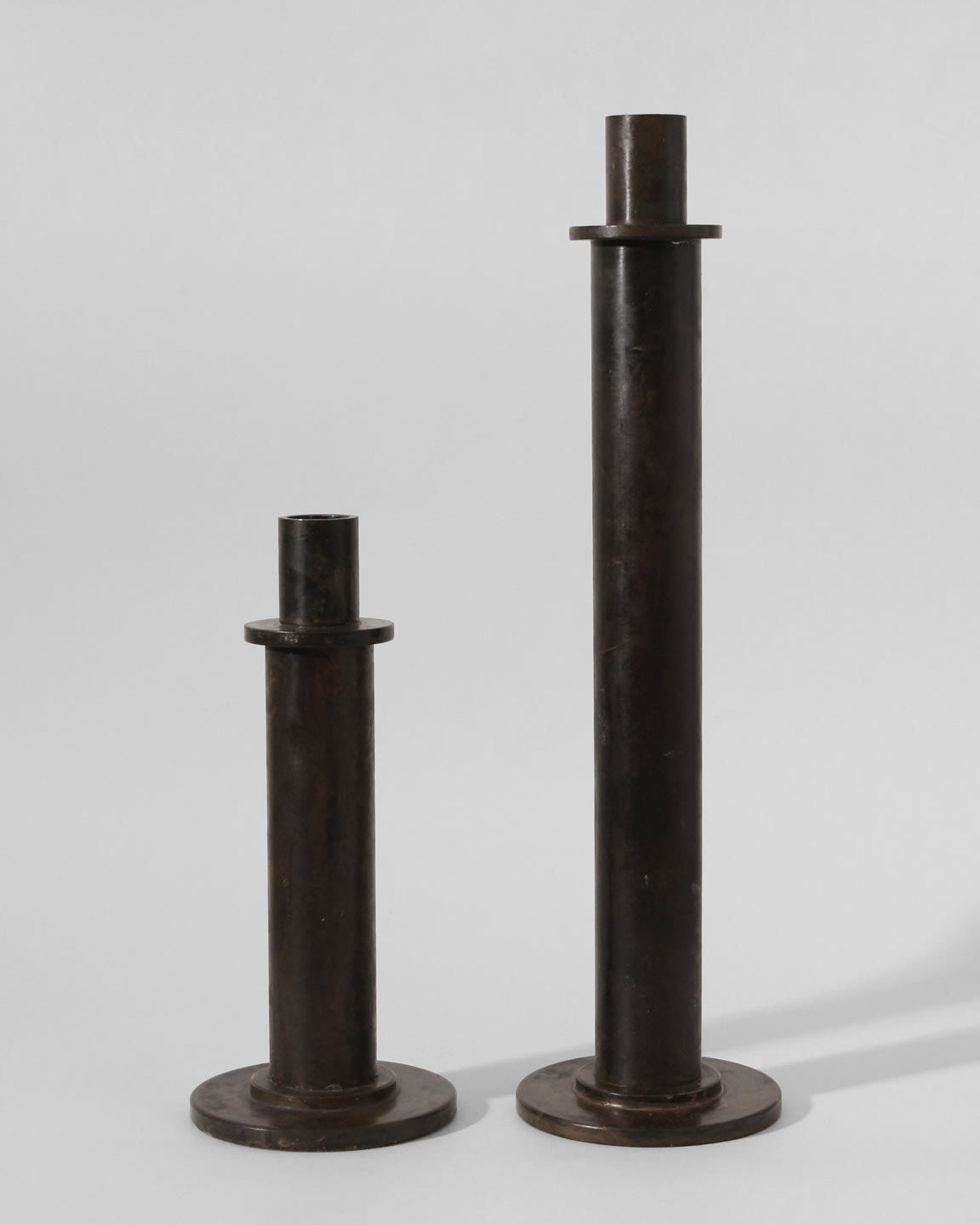The Pair of Brutalist Massive Iron Candle Holders by Vintage Stories, 1970s, features two upright iron cylinders of different heights with round bases and flat top discs, evoking vintage German candle holder design.