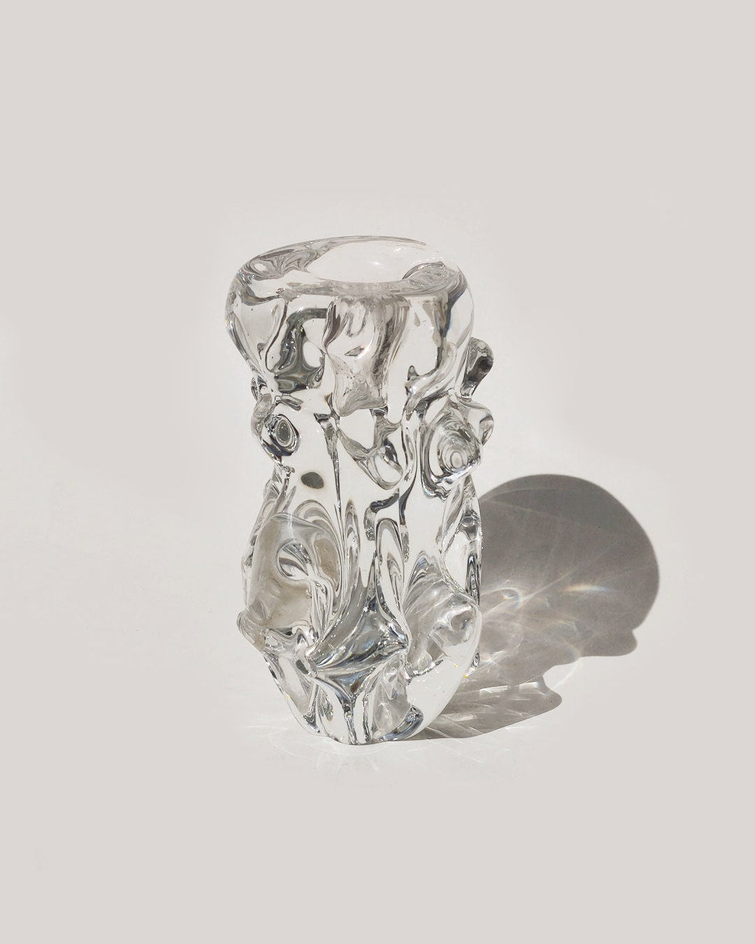 The Les Objoies Organic Glass Candle Holder, featuring a sculptural biomorphic design with abstract, swirling forms, rests on a light surface and casts a gentle shadow to the right.