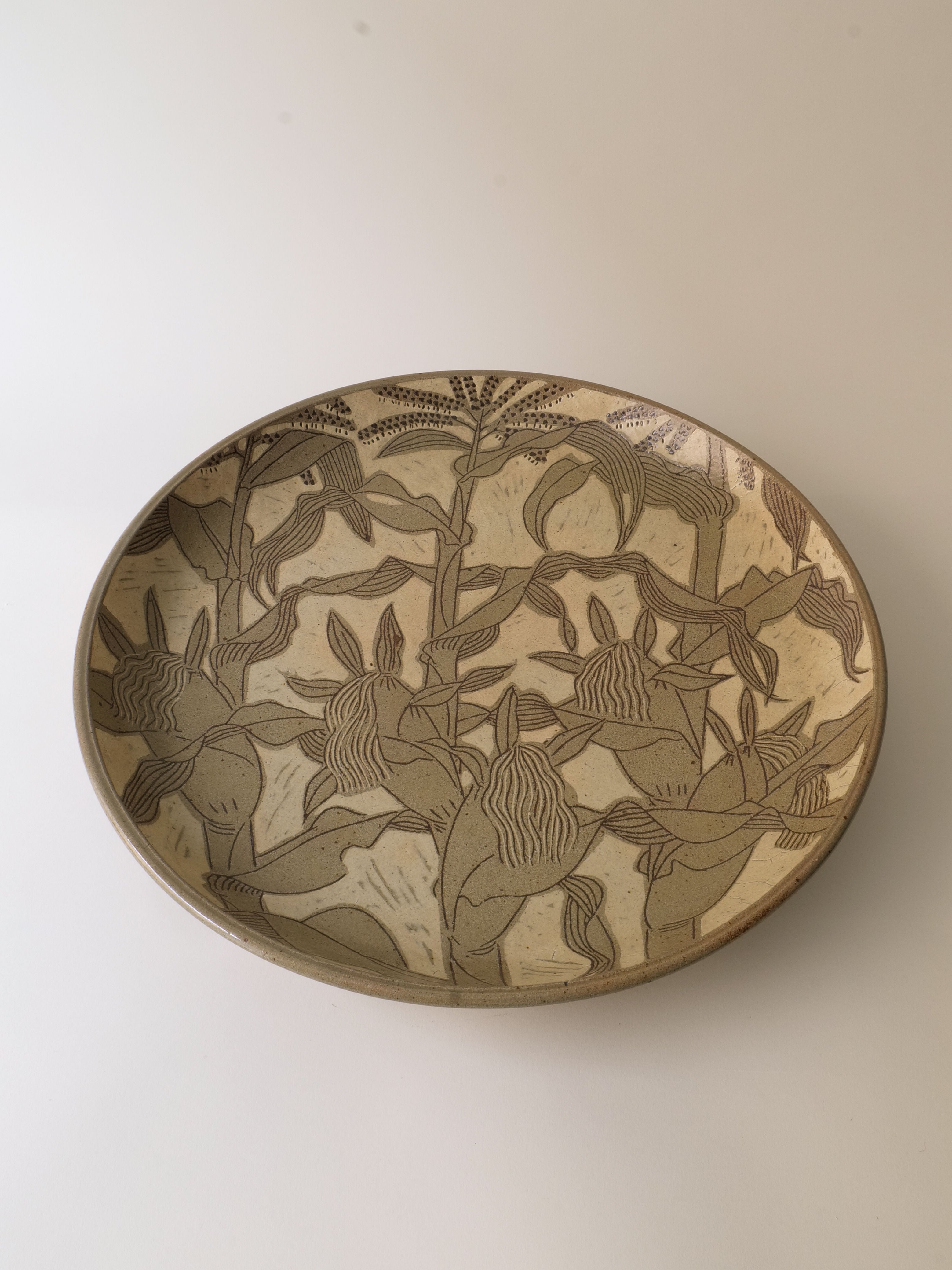 The Ceramic Plate Kenji Sugiura from Collection apart, crafted in Japan during the 1980s, features intricate etched floral patterns in earthy tones reminiscent of the Shōwa period. The designs cover the entire inner surface with stylized leaves and flowers, making it ideal for any Traditional Crafts Exhibition or as a standalone piece.