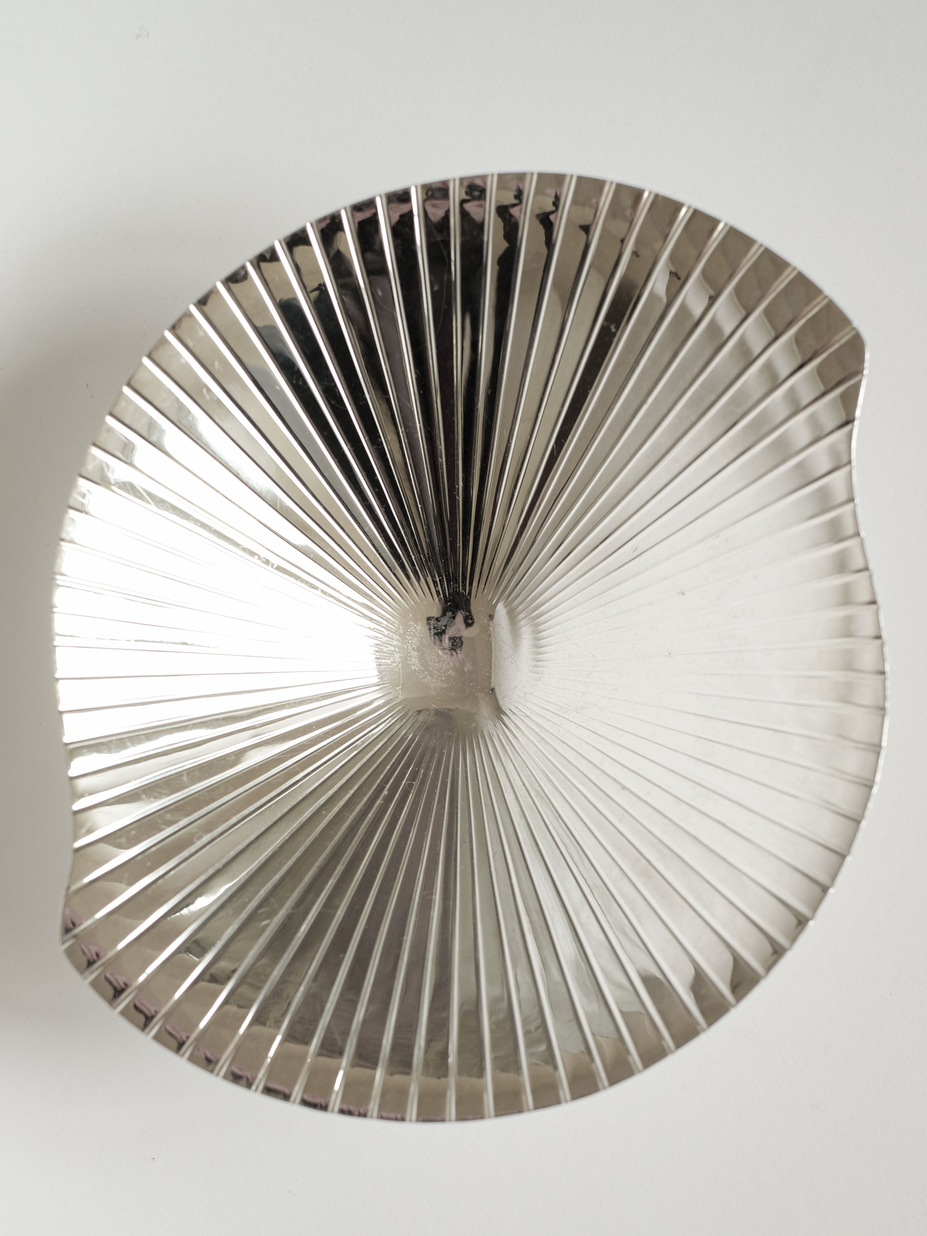 A shiny, metallic Silverplated Shell Dish by septembre studios with radial ridges and an organically curved edge, viewed from above on a white background—an elegant modern Mid Century design.