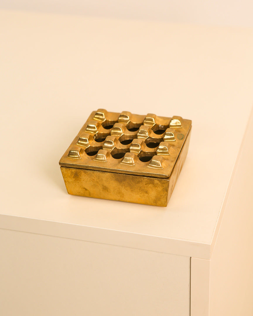 A square, elegant brass ashtray by Holger Bäckström & Bo Ljungberg (70s) for Treaptyque sits atop a light, minimalist table or cabinet.