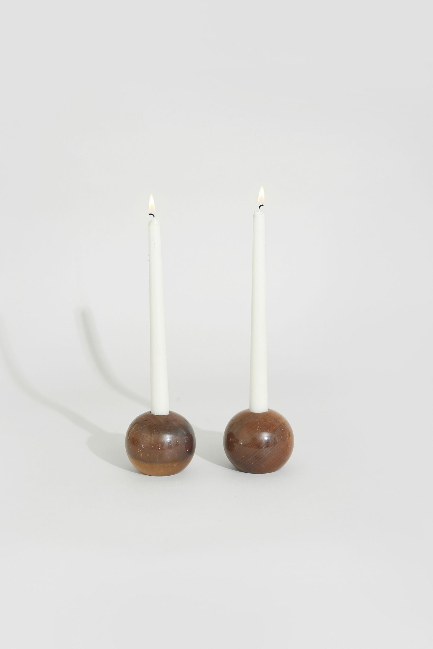 Two lit white taper candles in spherical walnut wood holders