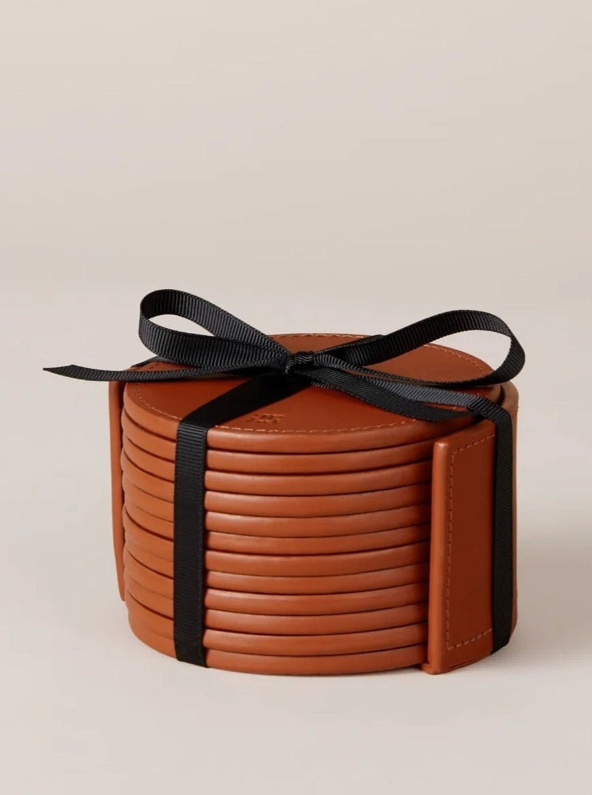 A set of round, vegetable tanned leather coasters from Paradise Row, elegantly tied with a black ribbon and neatly arranged against a neutral background.