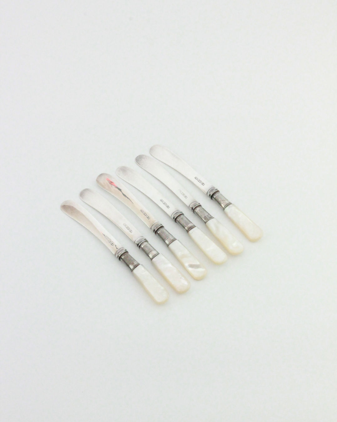 Six Boga Avante Shop Mother-of-pearl Butter Knives are arranged in a neat row on a plain white background.