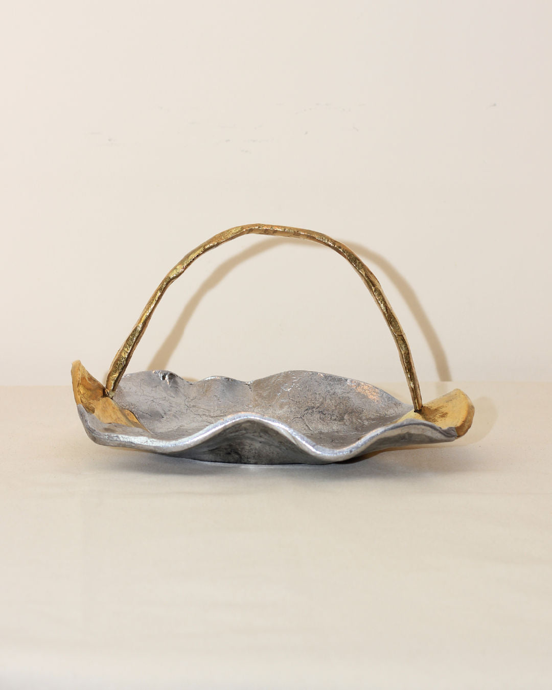 The Boga Avante Shop Brutalist Decorative Bowl pairs beautifully with a wavy-edged silver tray featuring gold accents and a curved, textured gold handle, creating a refined yet rustic display against a plain background.