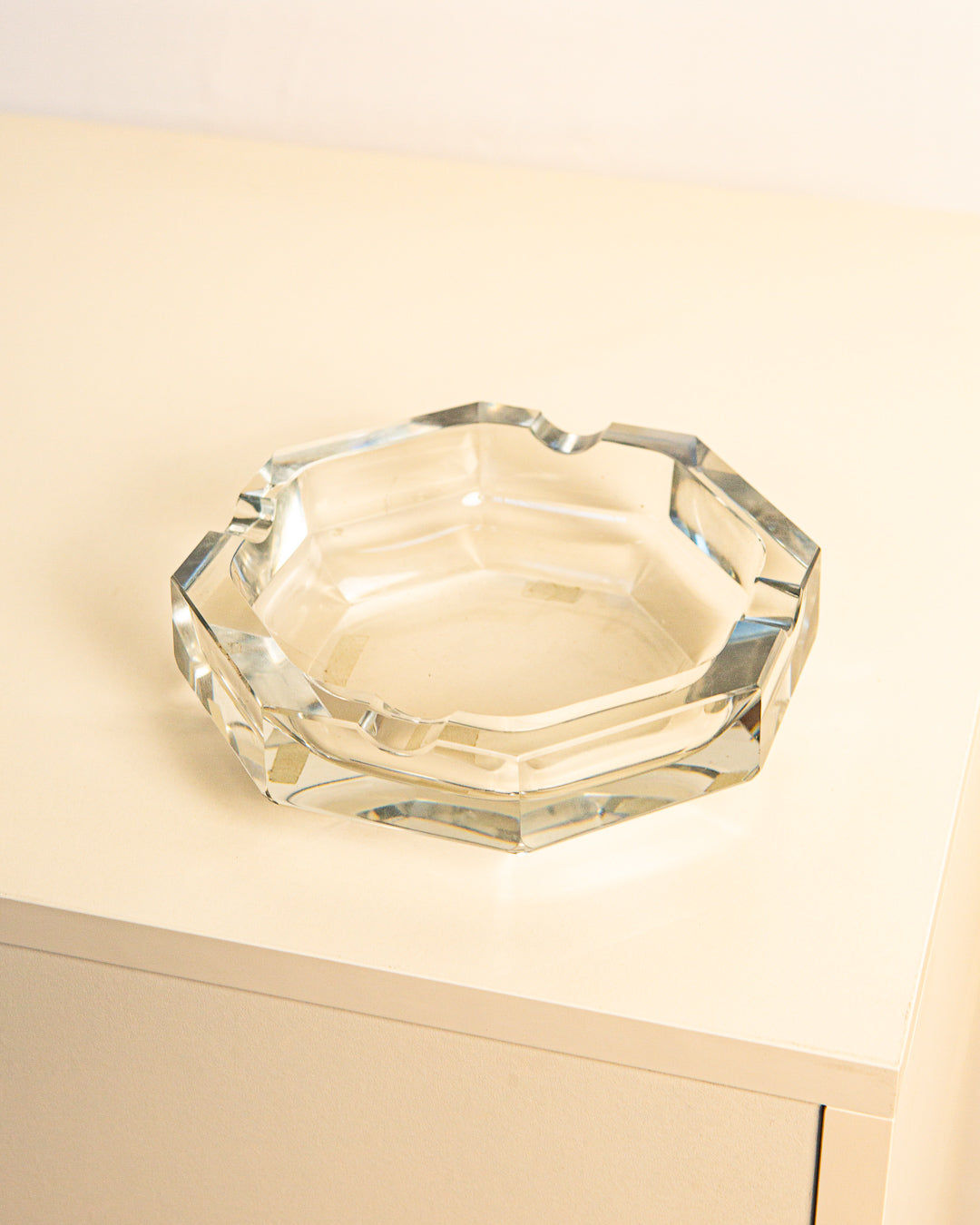 The Octagonal Glass Ashtray from the '80s by Treaptyque, featuring facet-cut edges and Italian craftsmanship, sits elegantly on a light-colored, minimalist surface.