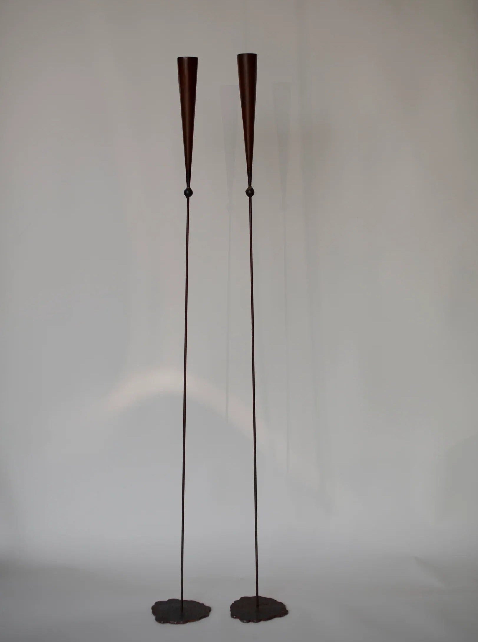 Two tall, slender, cone-shaped Set of Copper Candle scones by Pieter Spruyt 1980s with minimalistic design stand side by side on circular bases against a plain background. The lamps have long, thin stems and feature dark, metal finishes reminiscent of 80's signed pieces by CU-RA-TED.