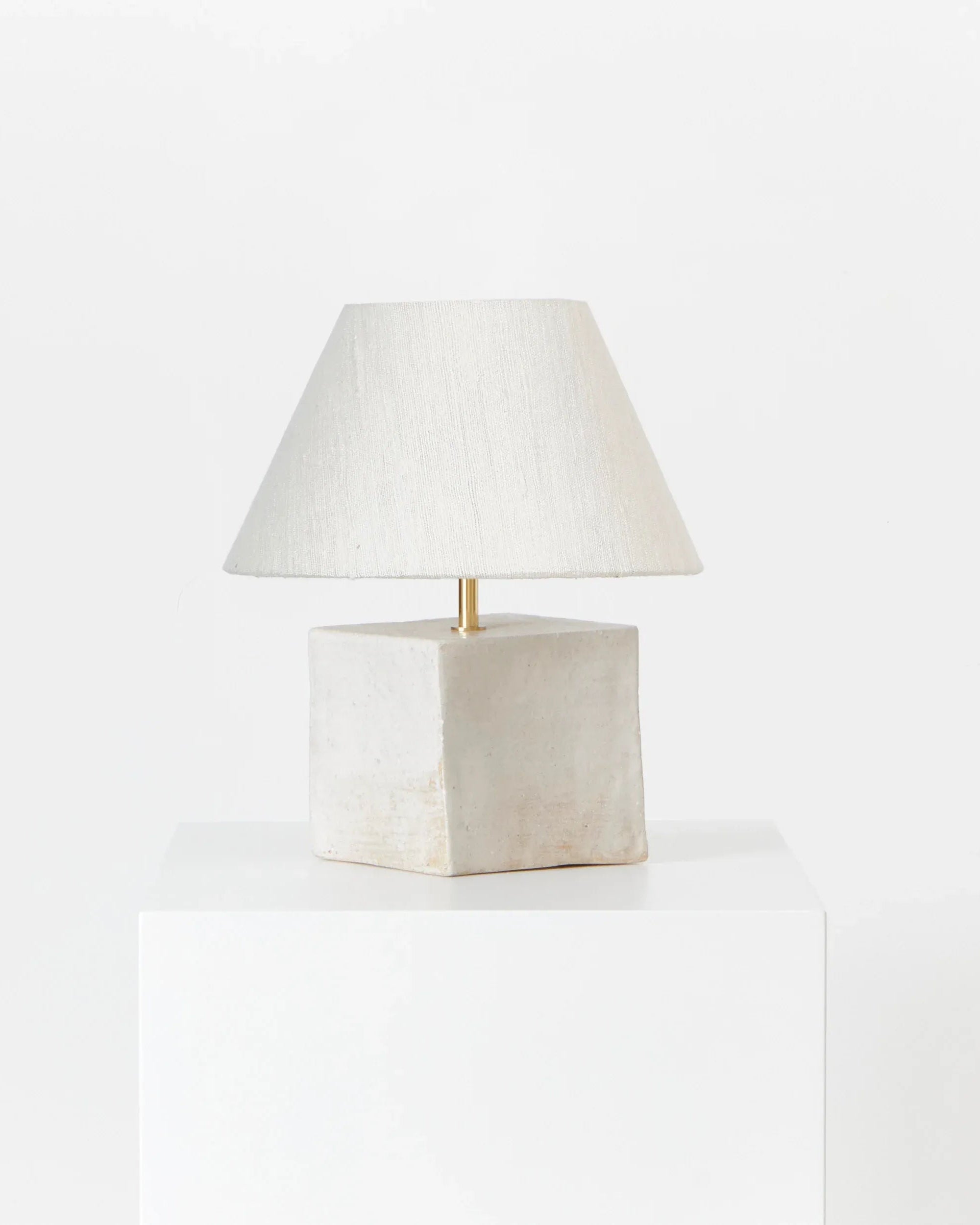 The Arouca Table Light White by Project 213A features a modern rectangular off-white ceramic base and wide cream fabric shade, displayed on a white pedestal against a plain white background.