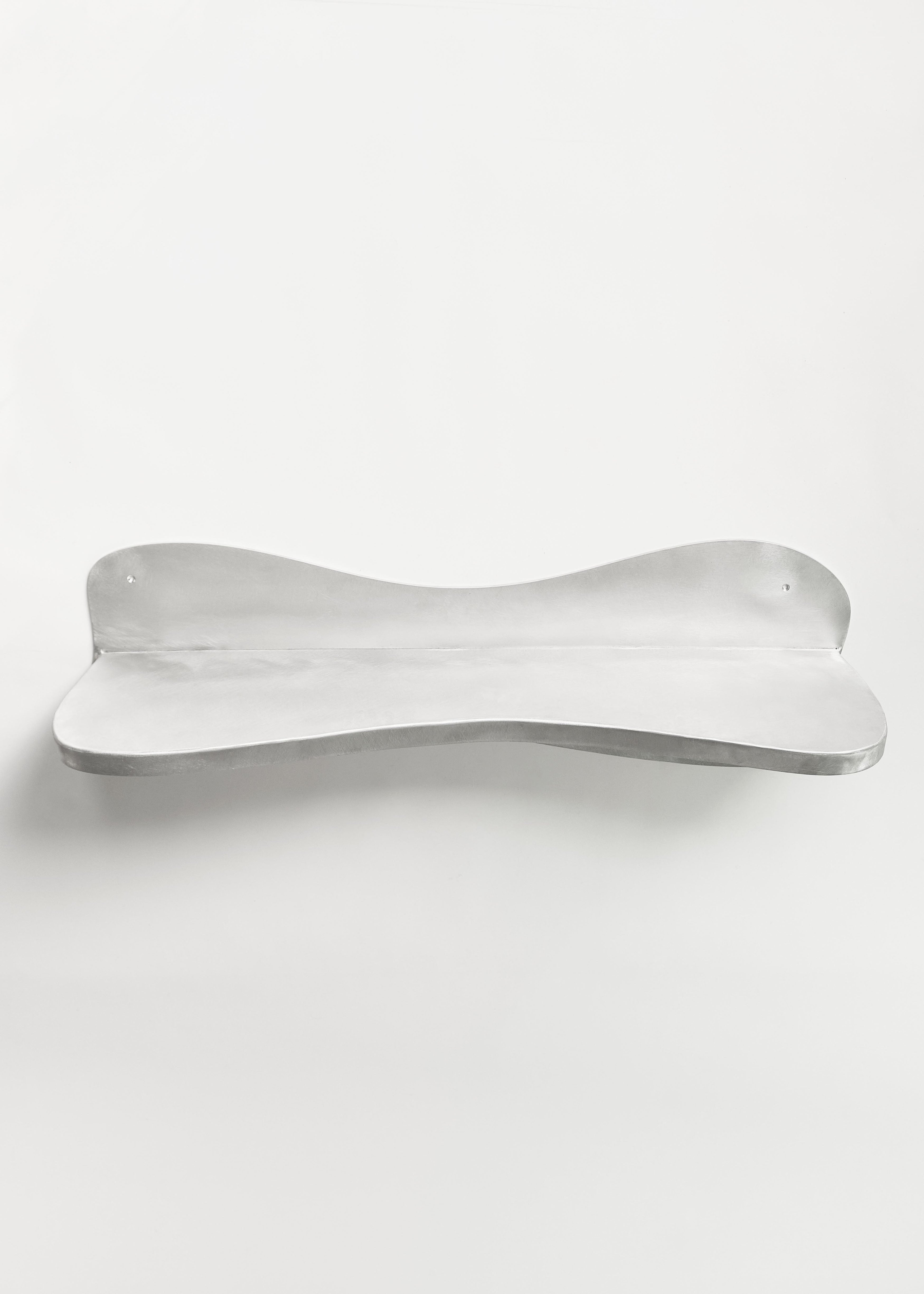 The handcrafted Big Shelf by Six Dots Design is a wall-mounted, minimalist piece made of sturdy metal with a gently curved design. Its silver finish reflects light for a sleek, modern look against a white background, creating a curated focal point.