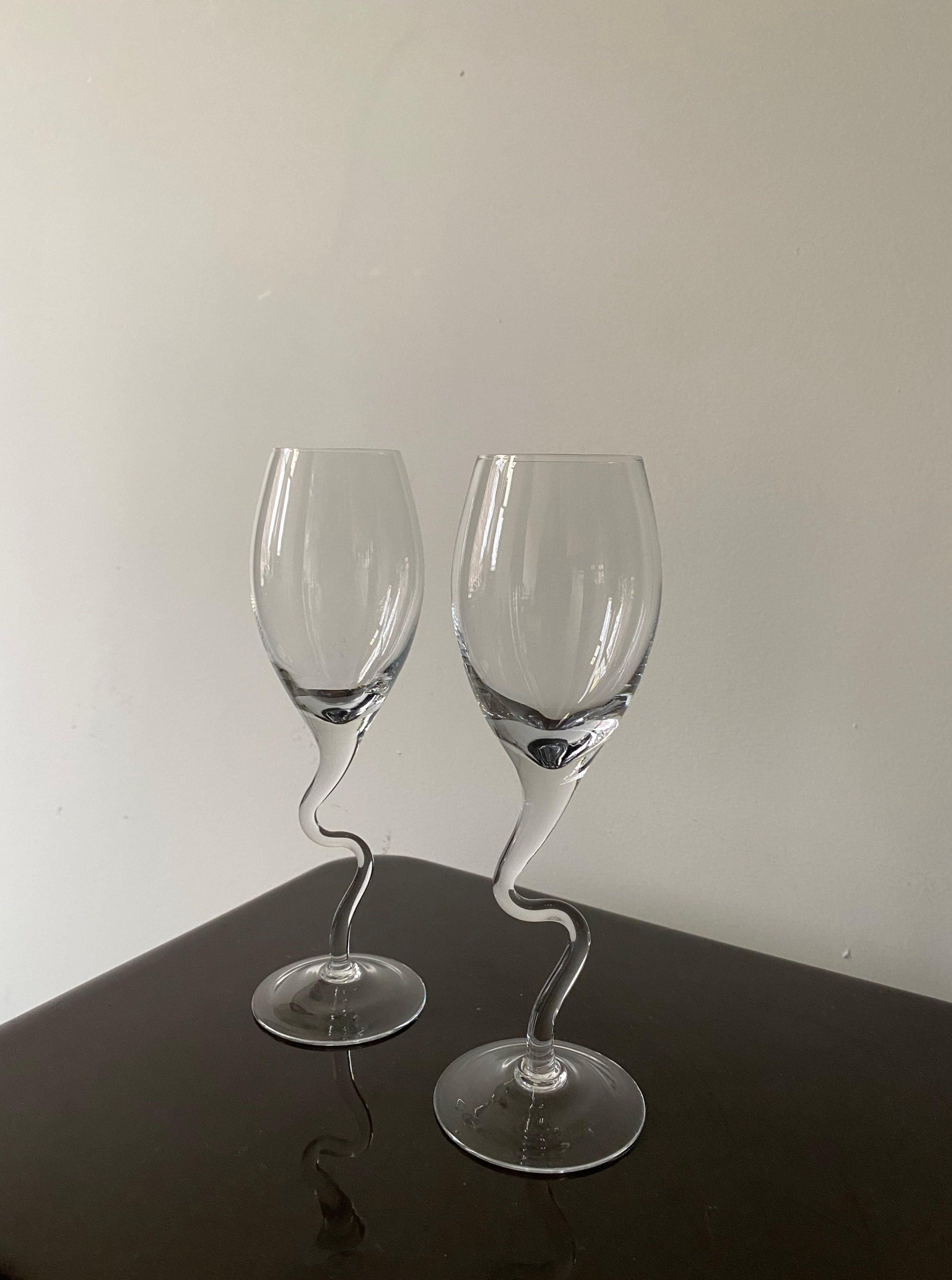 Two empty Les Objets Amsterdam Vintage 80s Champagne Glasses with unique twisted stems are placed on a dark table against a light grey wall.
