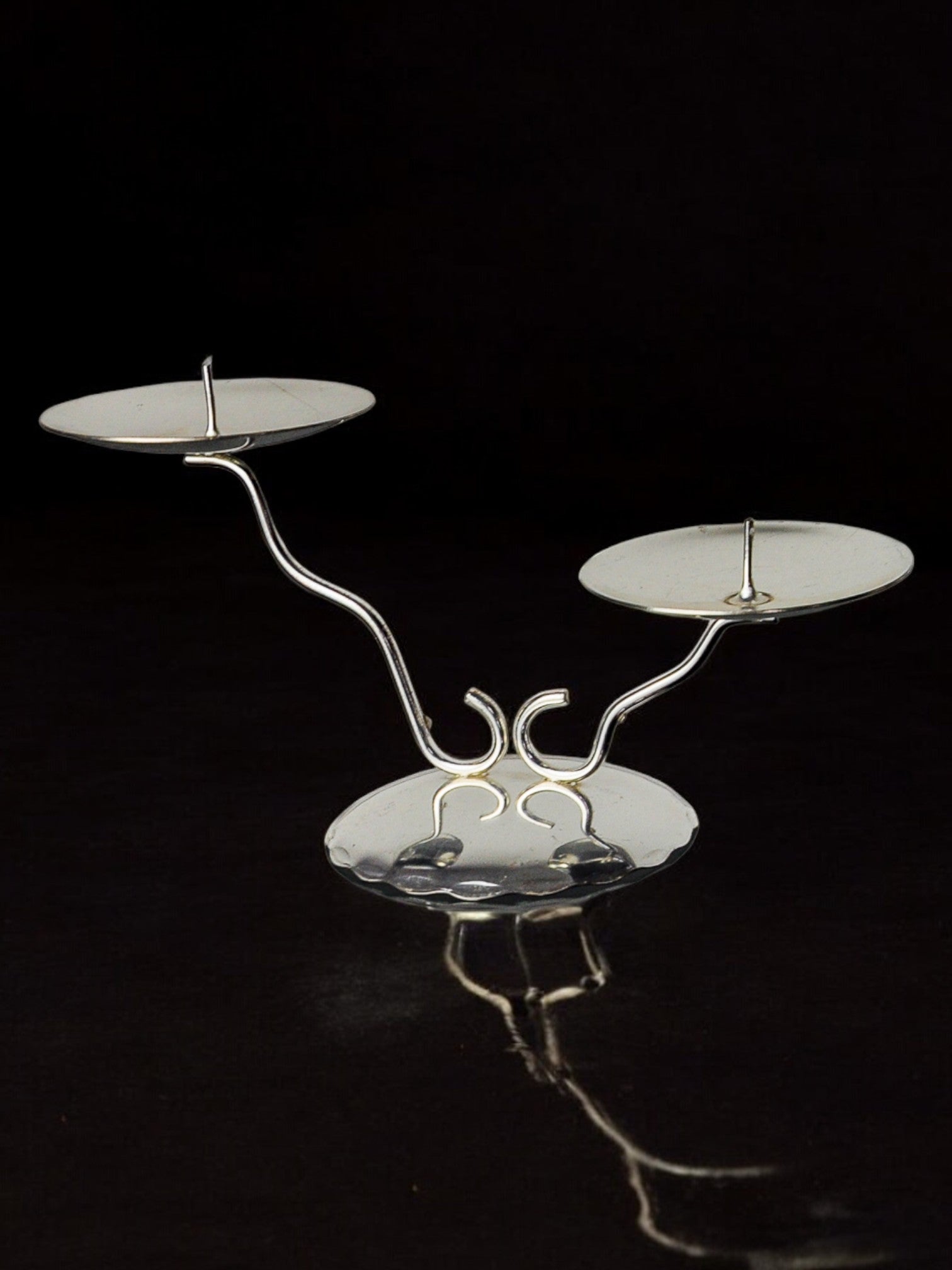 The Art deco 2-flame candlestick by Malamar Studio, Spain, 1980, features a modern minimalist design with sleek metal lines and curved stems, adding a sophisticated touch to any décor, set against a striking black background.
