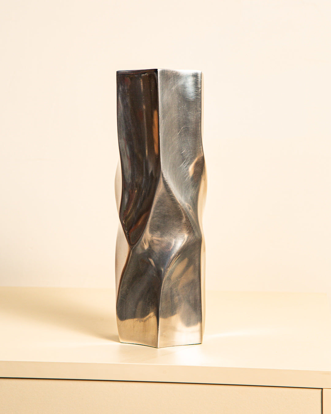 The Treaptyque Large Italian “Hexagon” Vase 80s, a tall modern silver cast aluminum piece with a twisted geometric design, stands on a light surface against a plain off-white background.