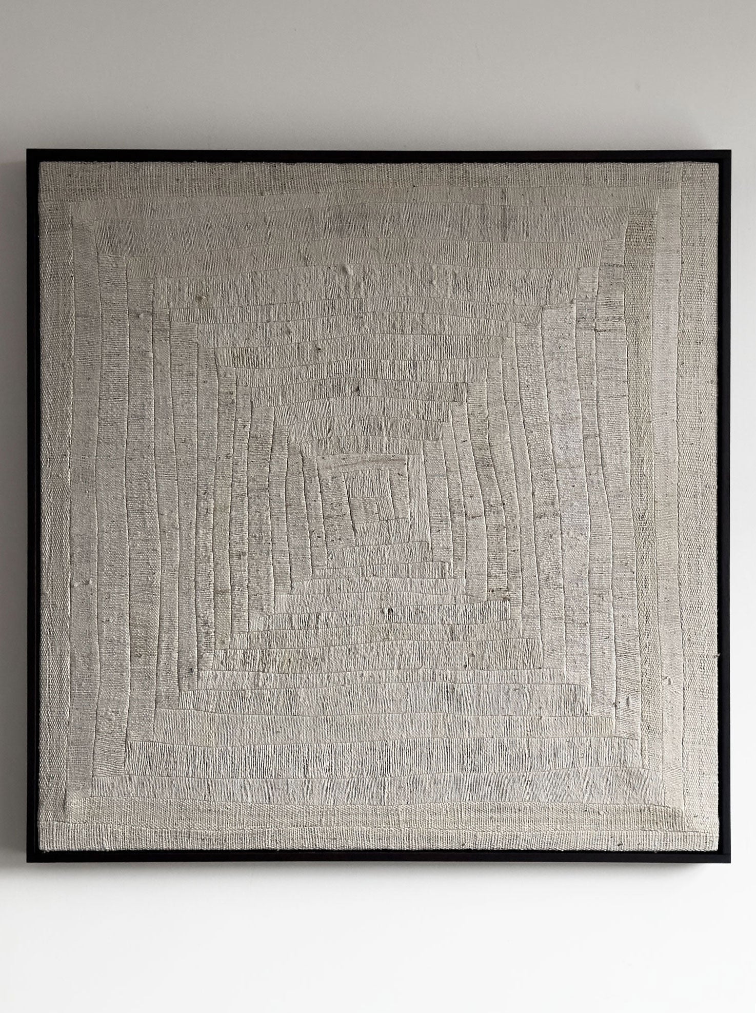 The "Mending II, 2024" artwork by Bec Kirby is a textured, handwoven kapok fiber piece showcasing a complex geometric design with intersecting vertical and horizontal lines that form a central square pattern. The log cabin patchwork is elegantly framed in black solid oak and beautifully mounted on a neutral-colored wall.