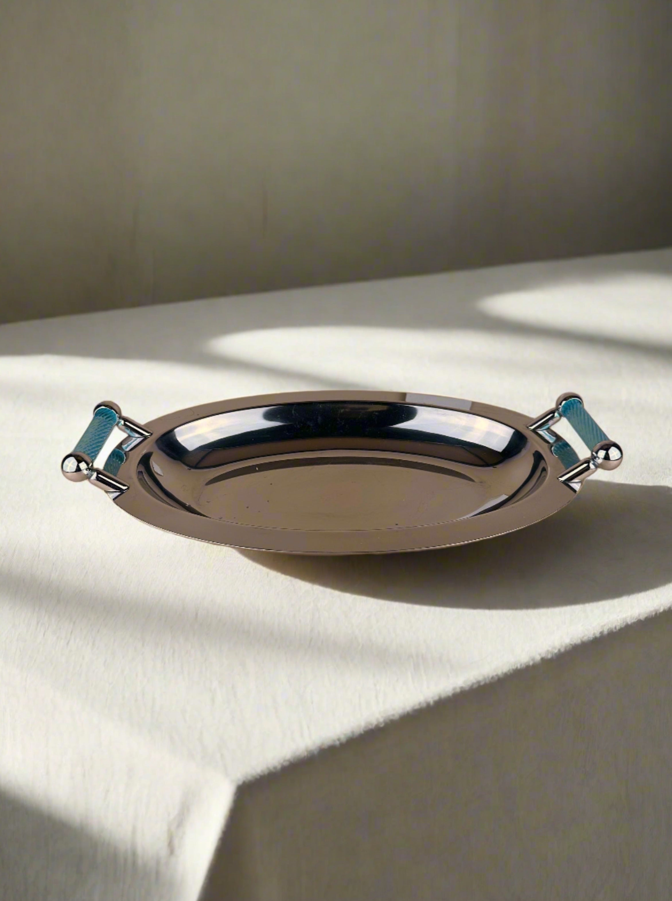A polished silver-coloured Dodo Vintage Italian 1980s Tray with azure blue handles on either side is placed against a neutral beige background. The ribbed texture of the handles adds a touch of style to the sleek, reflective surface, evoking an elegant piece from Italy 1980s.