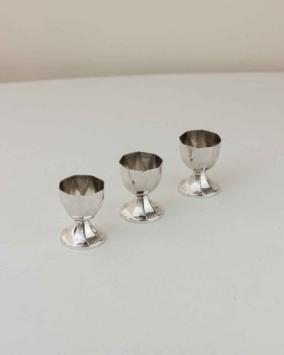 Three vintage silver egg cups arranged in ascending size on white surface