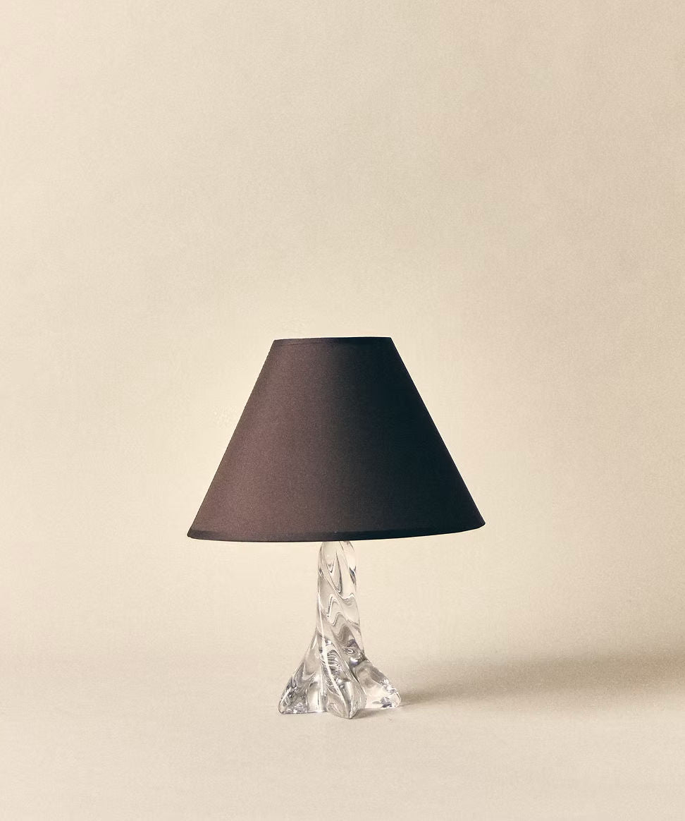 The SÒLER 'Ostuni' Table Lamp features a transparent sculpted glass base and a conical chocolate shade, displayed against a plain light beige background.